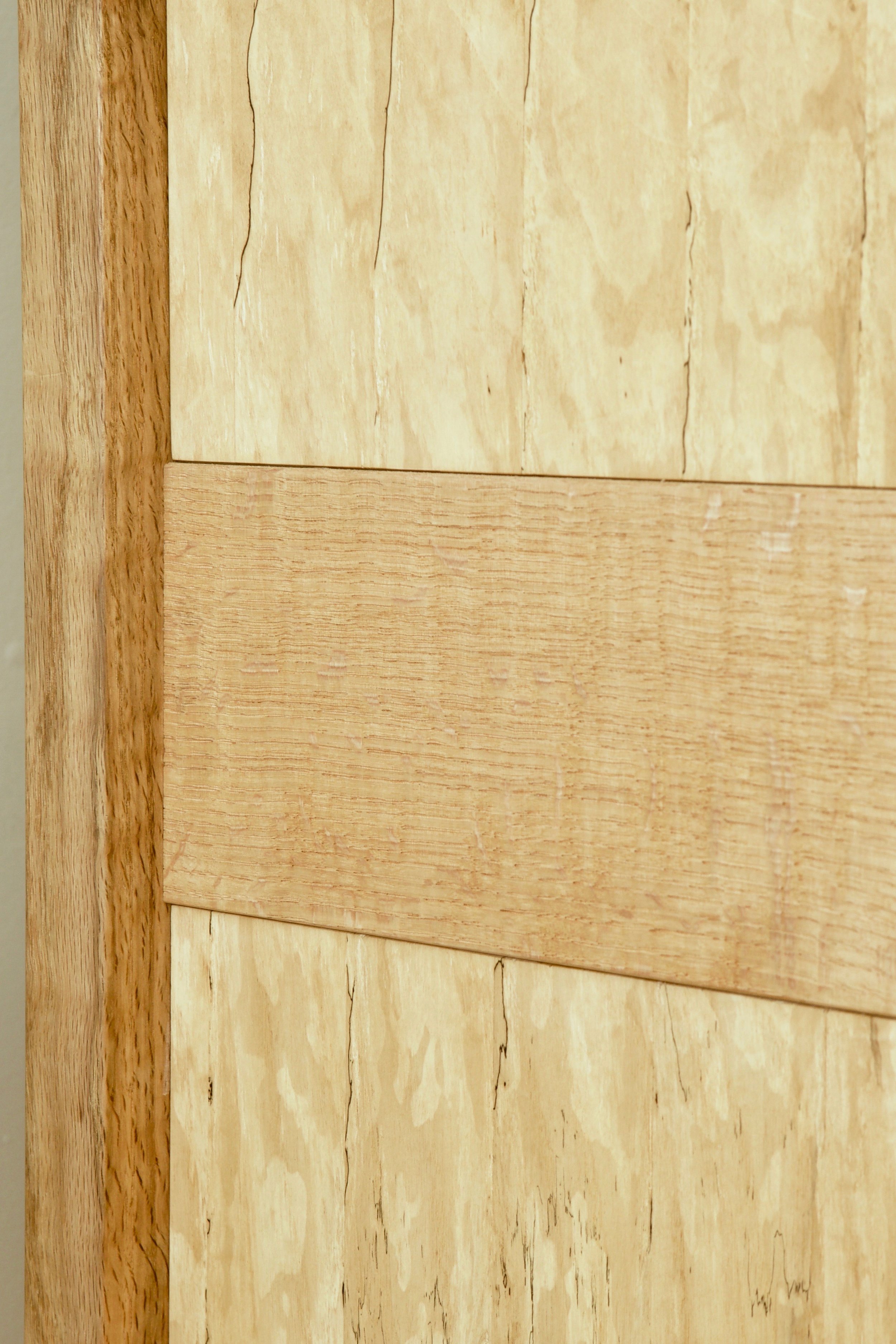 The bookcase has two complementary wood species, quartersawn red oak and spalted persimmon. The red oak shelves are veneered, and the legs and rails are solid. The persimmon floating panels are all solid, laid up in the “recorded” or sequential slip match pattern.