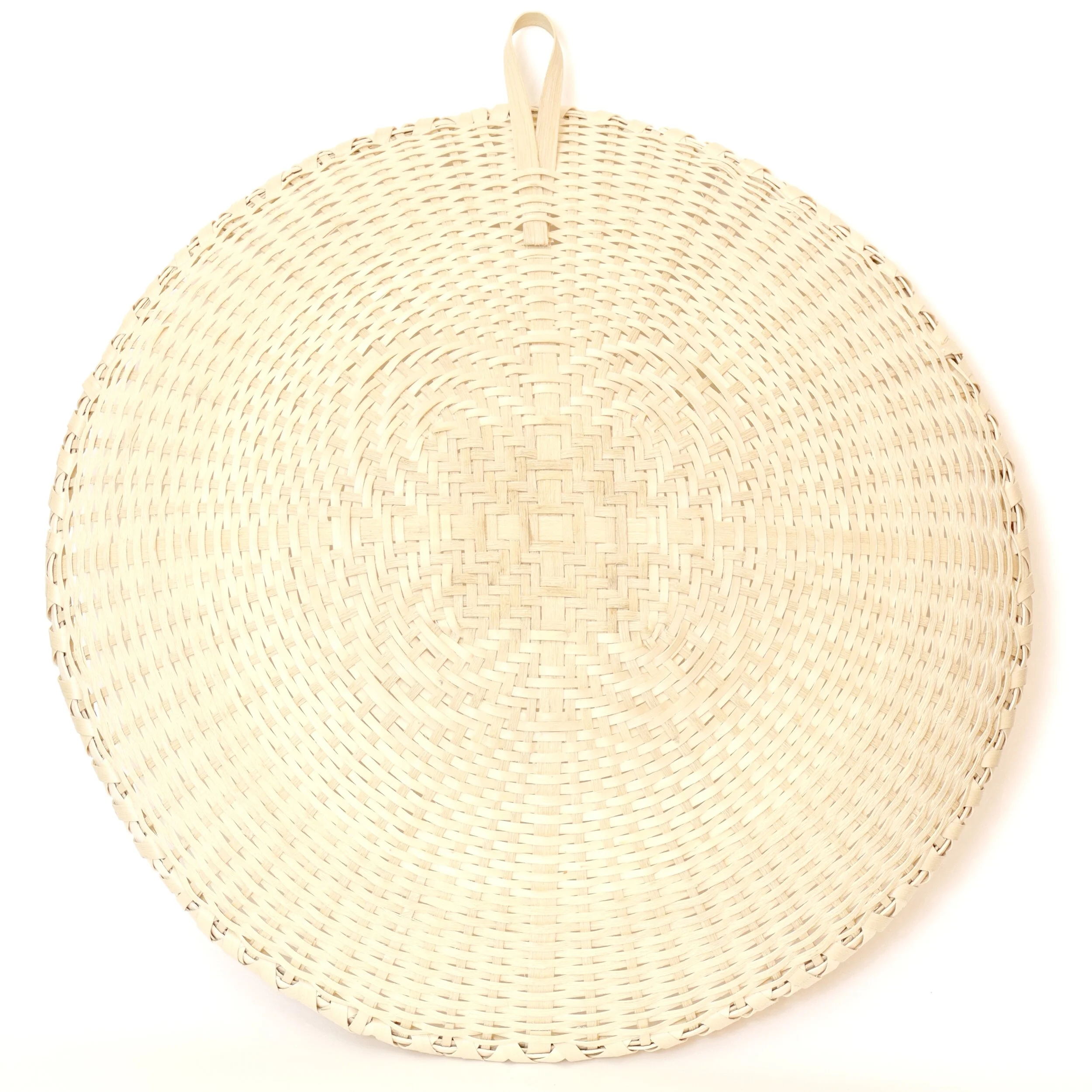  This white ash winnowing tray, with a white oak splint hanging hook, was inspired by the Shaker “quatrefoil” weaving pattern, which yields the clover-shaped pattern at the center of this basket. 