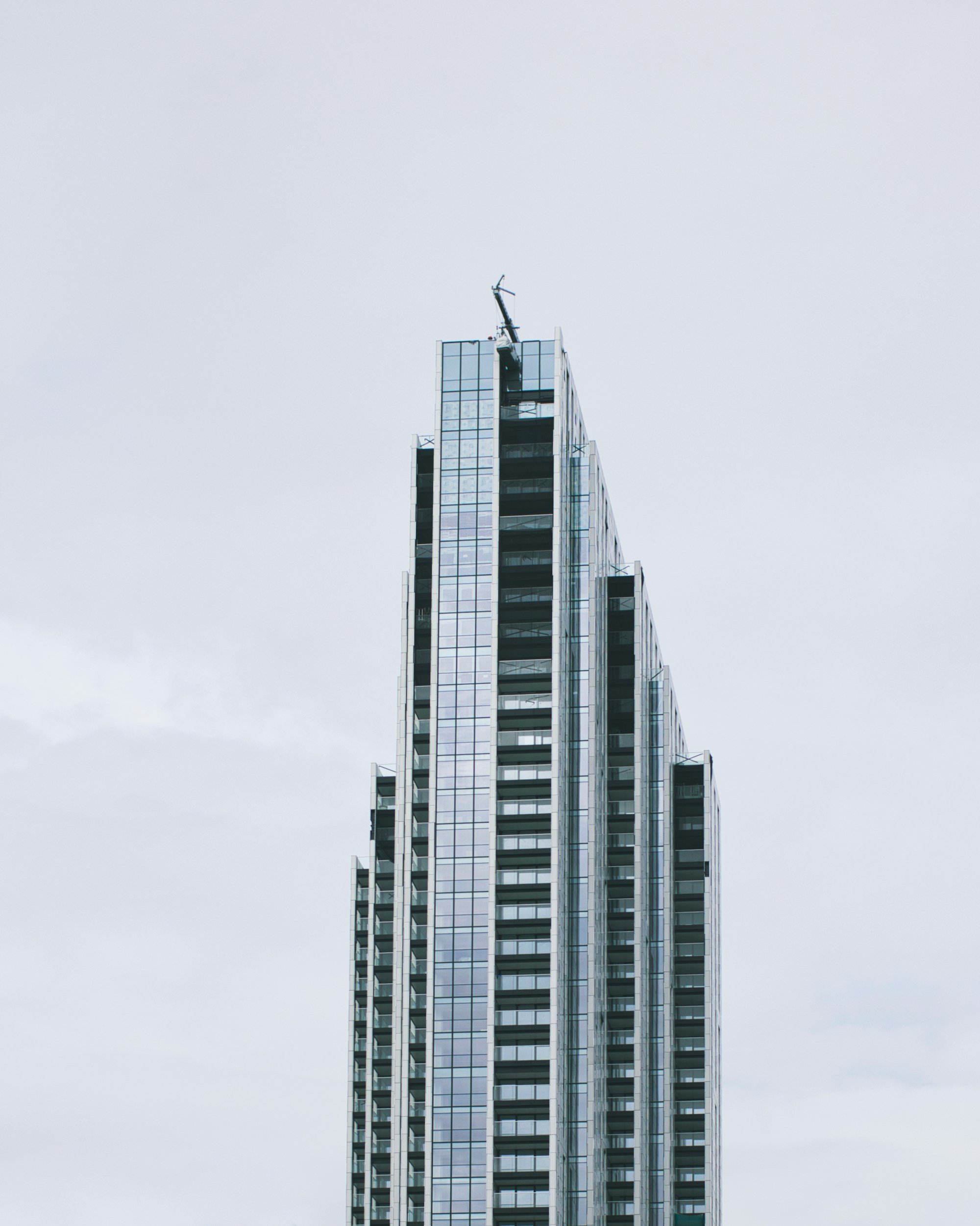 Tall modern skyscraper with glass windows and a construction crane on top, set against an overcast sky.