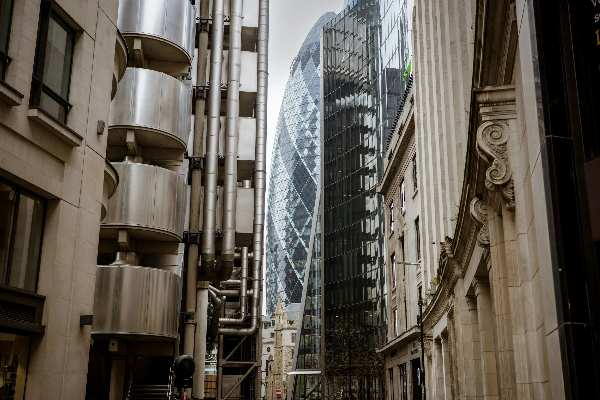 Street view with diverse modern and classical architecture, including a glass skyscraper with a twisted design, an older building with ornate moldings, and a curved building with metal balconies.