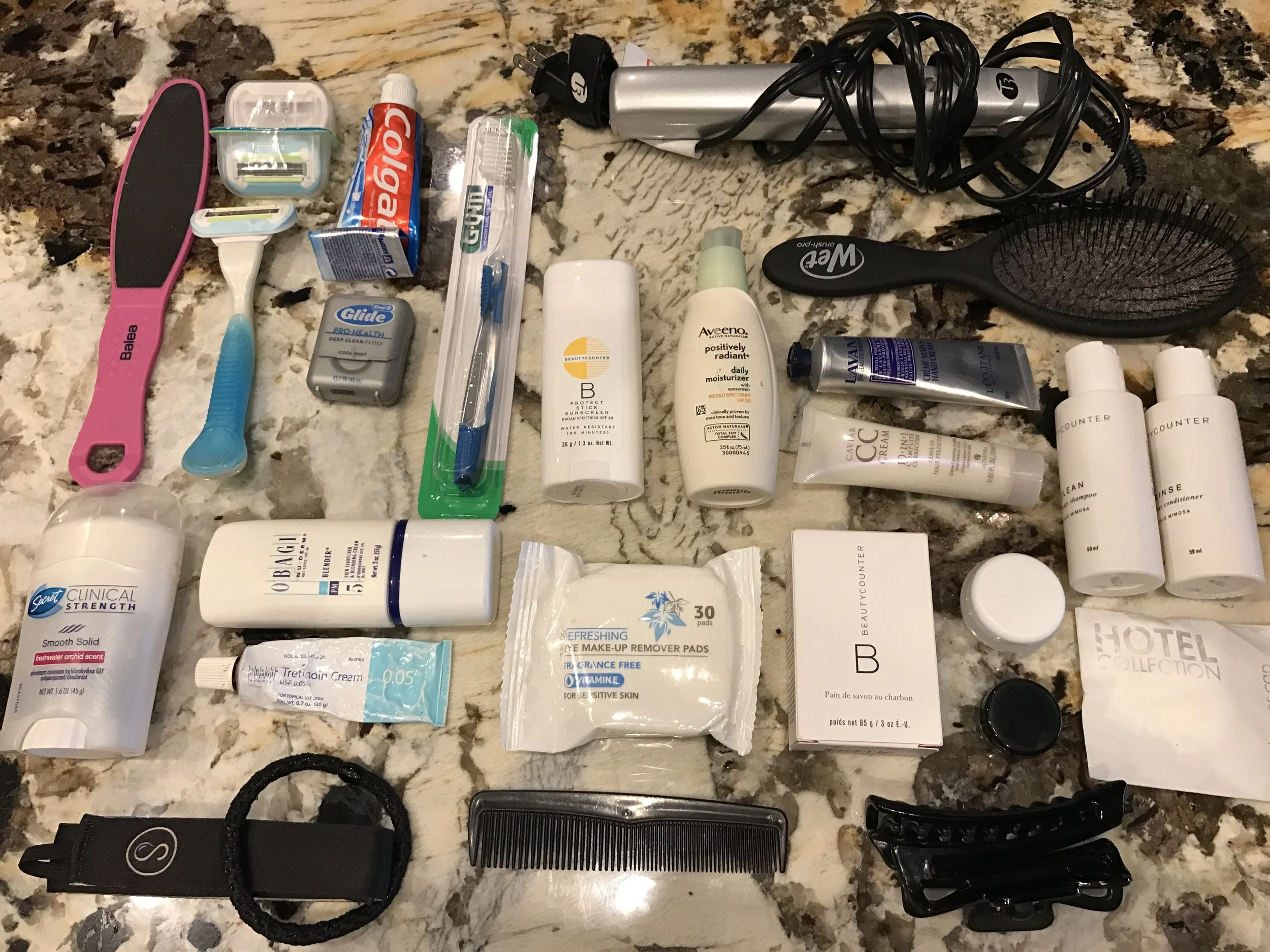 Deodorant, foot scrubber, razor, toothpaste, floss, toothbrush, Beautycounter sunscreen stick, Aveeno daily moisturizer, flatiron, brush, L'Occitane hand cream, CC leave-in hair treatment, Beautycounter shampoo/conditioner, shower cap, shine serum, Beautycounter charcoal cleansing bar, hair clip, comb, makeup remover pads, Obagi tretinoin and lightener, hair elastic/headband
