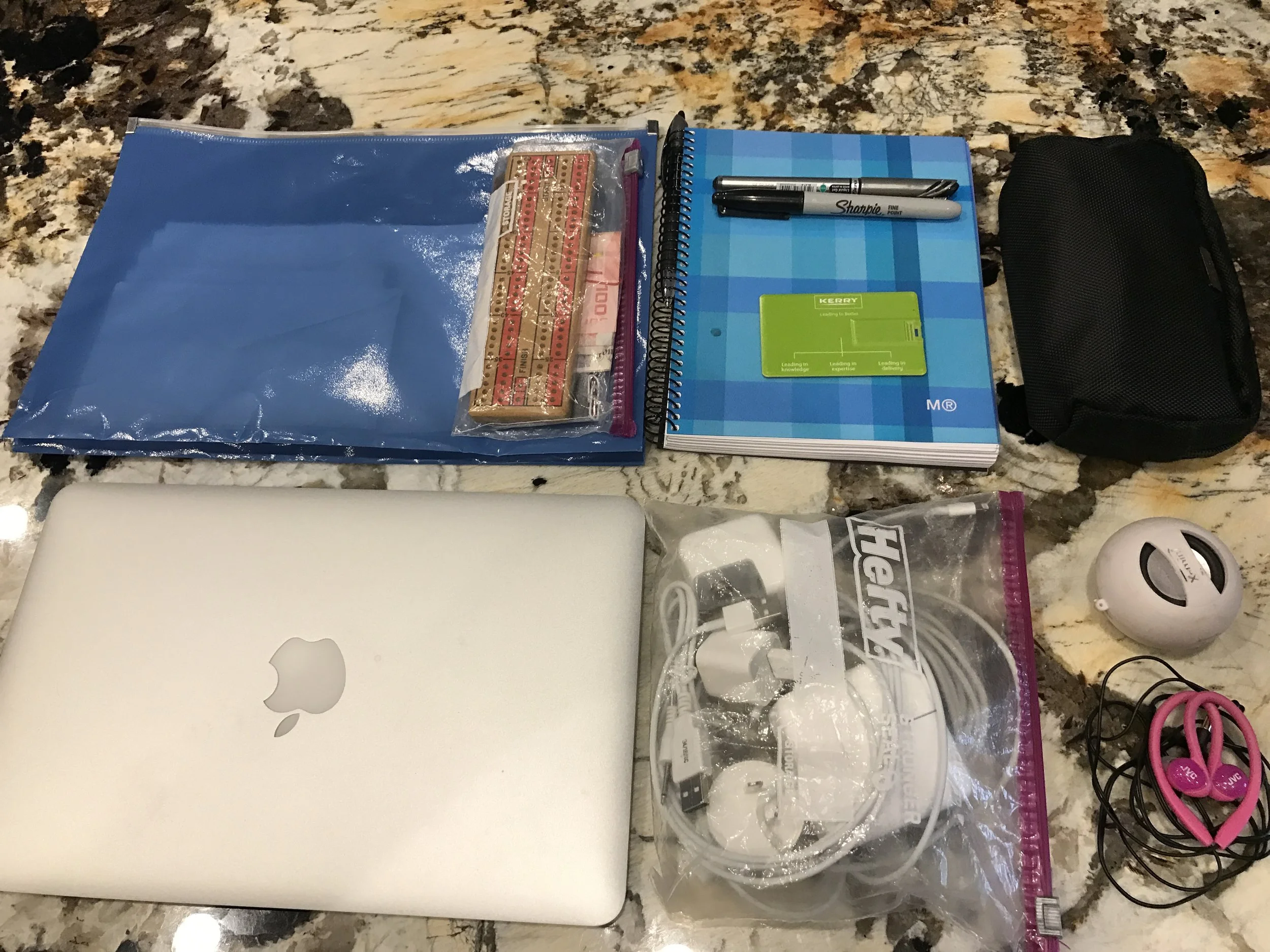 Folder with passport/currency/travel documents/cribbage board, Macbook Air 11 inch, cords/plugs, memory stick, pens, notebook, miscellaneous office supplies/first aid kit (black pouch), mini speaker, earbuds, iPhone 7 (not shown)