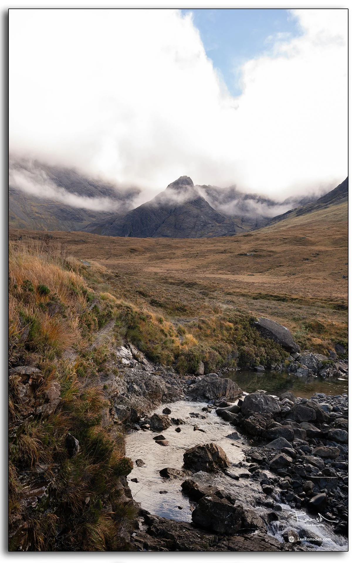 View towards the Cuillin mountains from the Fairy Pools on the Isle of Skye, with mist rolling over rugged peaks and a rocky stream in the foreground.