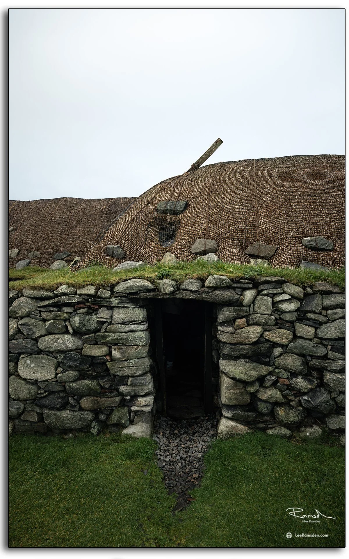 Traditional stone and thatch blackhouses at Gearrannan on the Isle of Lewis, Scotland, showing restored crofting homes surrounded by green grass and moody skies