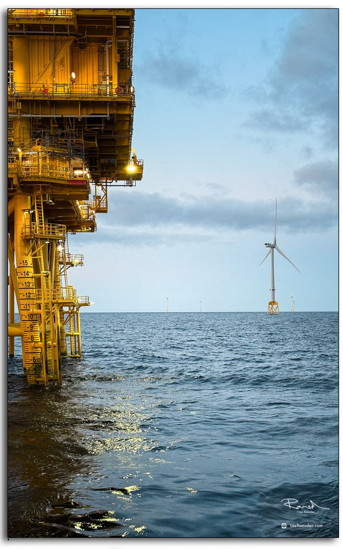 ndustrial offshore platform with turbines on the horizon and sea reflections at dusk.