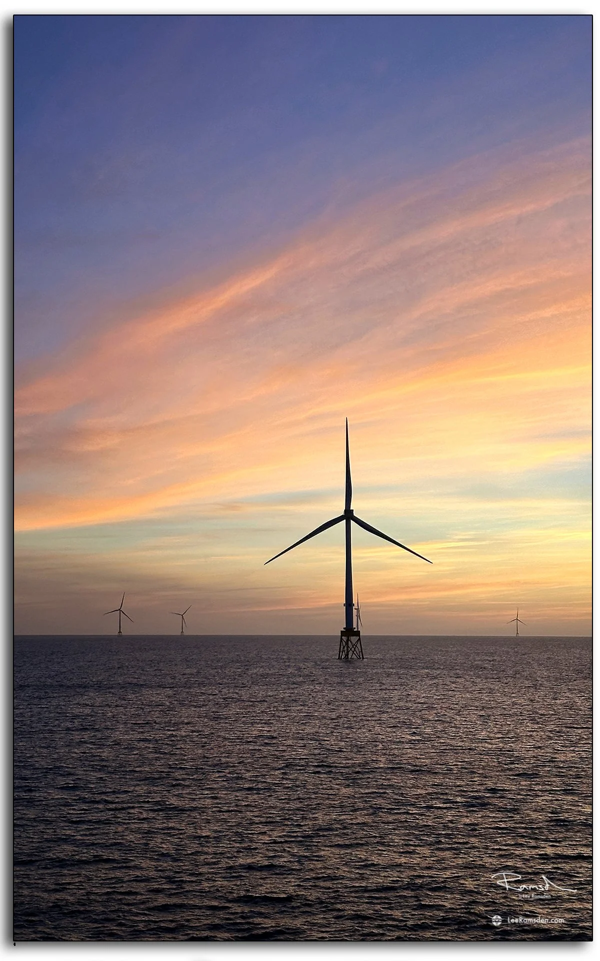 Close-up of turbines silhouetted against a vivid golden sky at sea.
