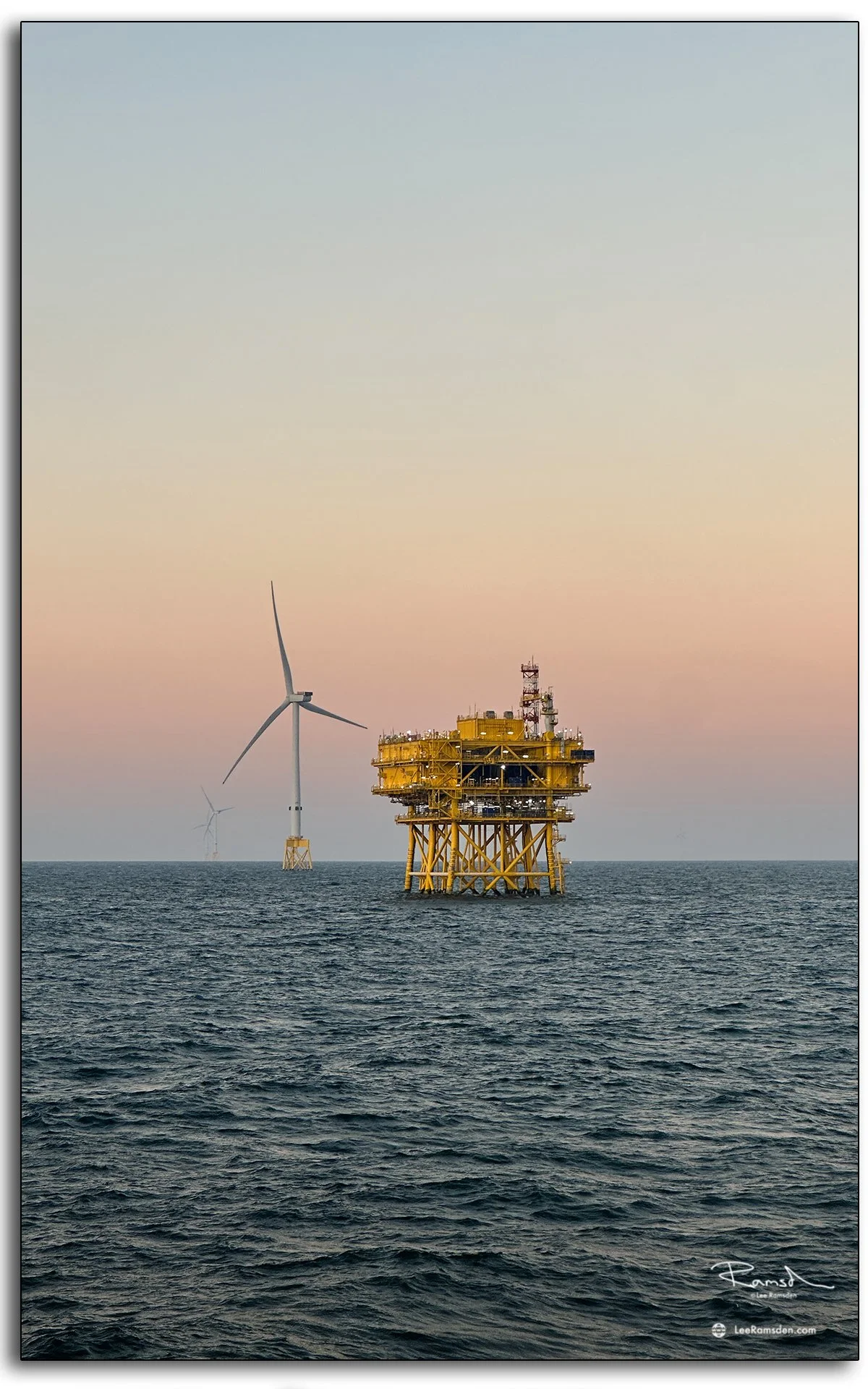 Offshore substation and wind turbine at sunset with pastel sky and calm sea.