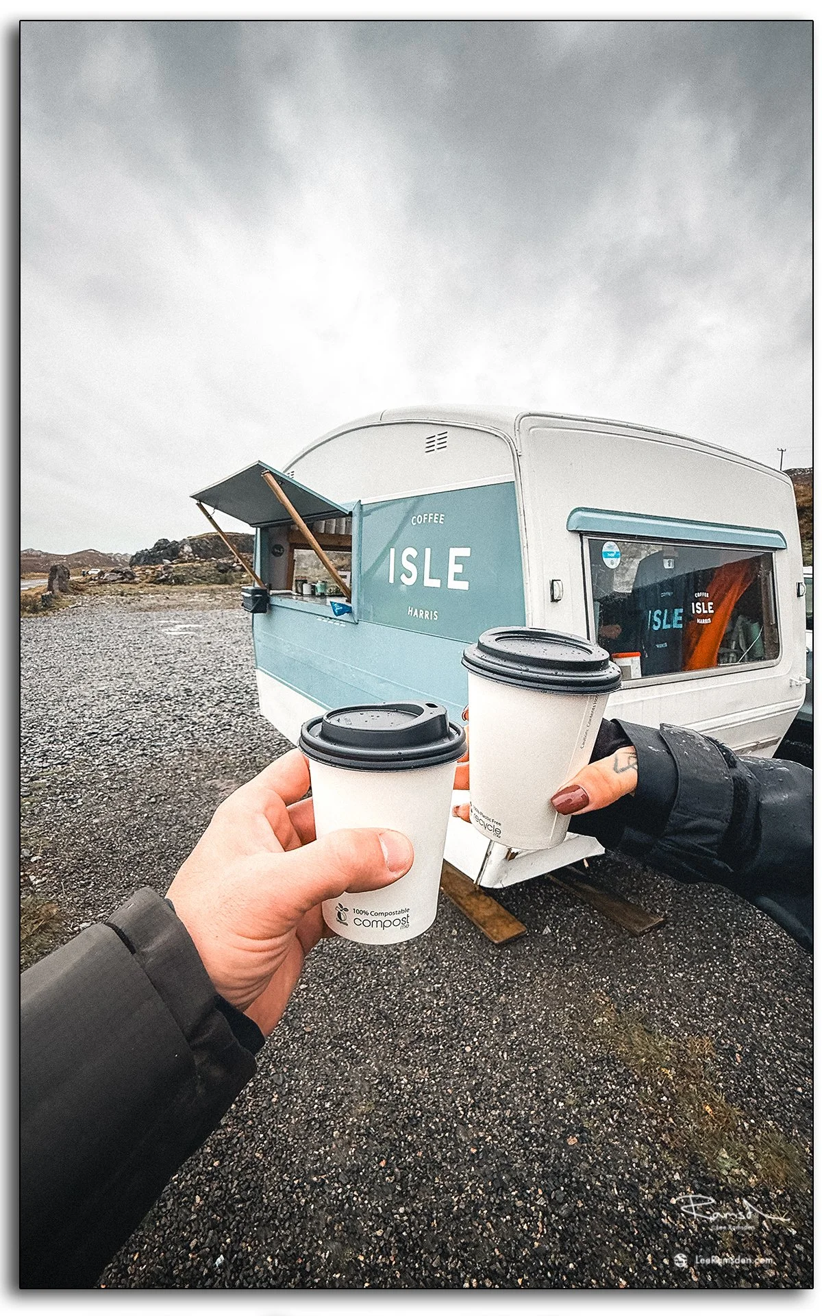 Two takeaway coffees held up in front of the Isle Coffee van on the Isle of Harris, Scotland, during a rainy Hebridean morning.