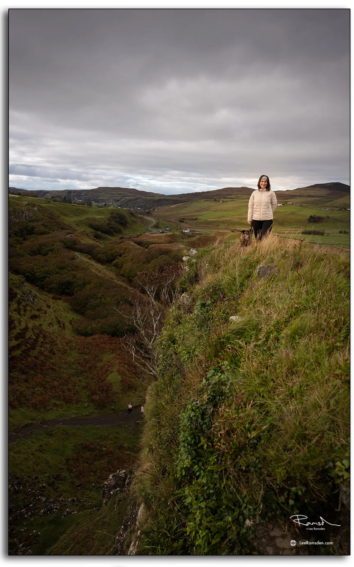 Woman standing on a rocky path overlooking the Fairy Glen on the Isle of Skye, Scotland, with sunlight highlighting the hills behind