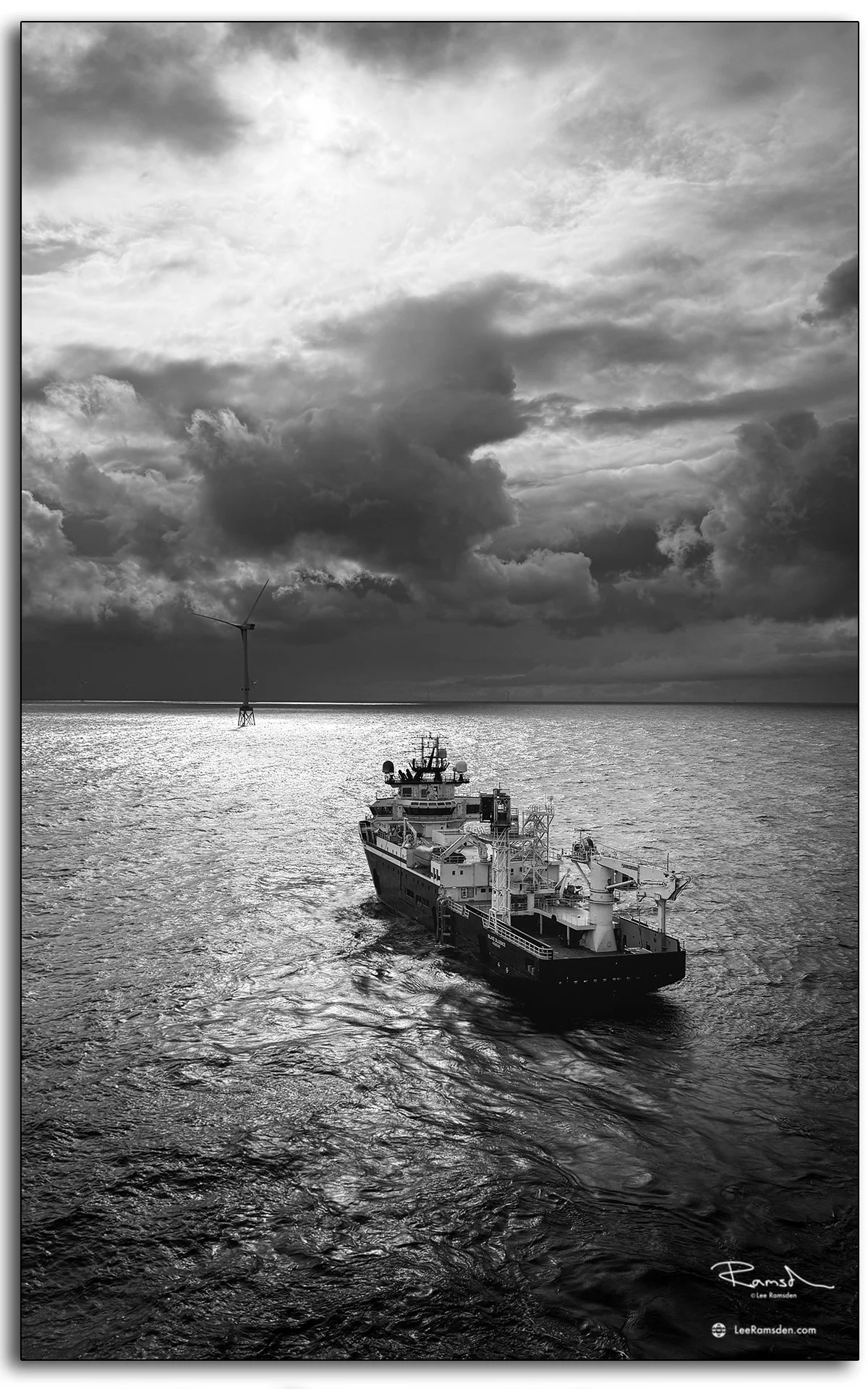 Moody black and white seascape of Island Diligence vessel with offshore wind turbine in the North Sea.