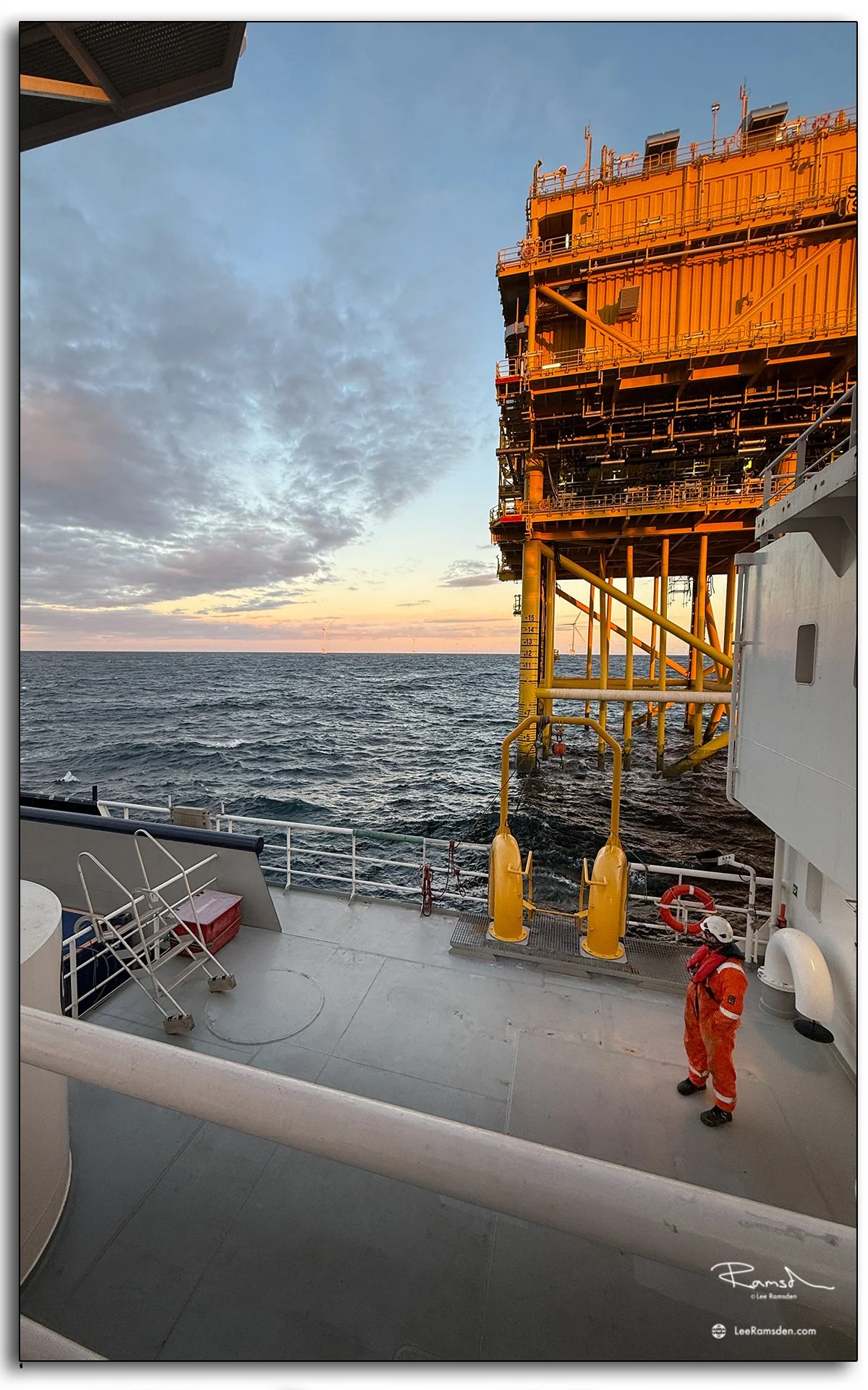 Offshore substation platform viewed from vessel deck at golden hour.
