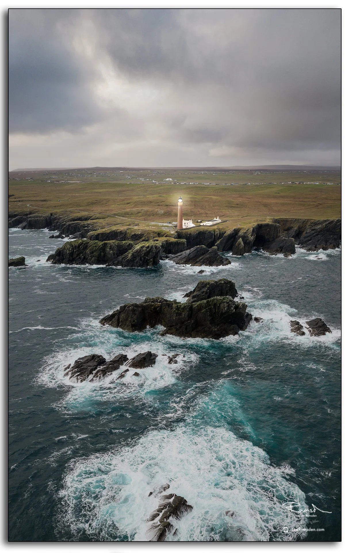 Aerial view of the Butt of Lewis lighthouse on the Isle of Lewis, Scotland, surrounded by dramatic cliffs and crashing Atlantic waves under moody skies.