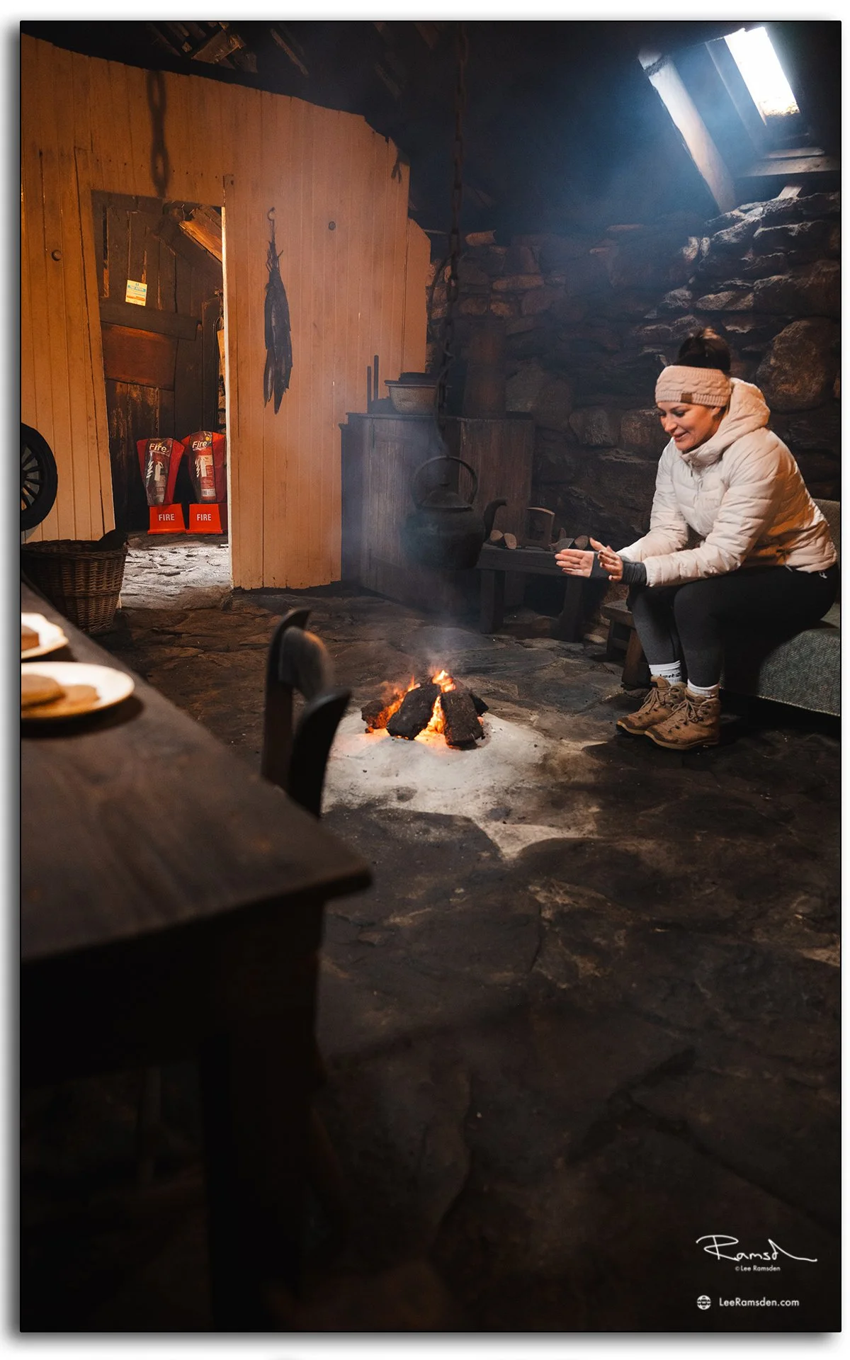 Interior of a traditional blackhouse at Gearrannan on the Isle of Lewis, Scotland, showing an open fire, hanging kettle, and rustic stone-and-wood construction
