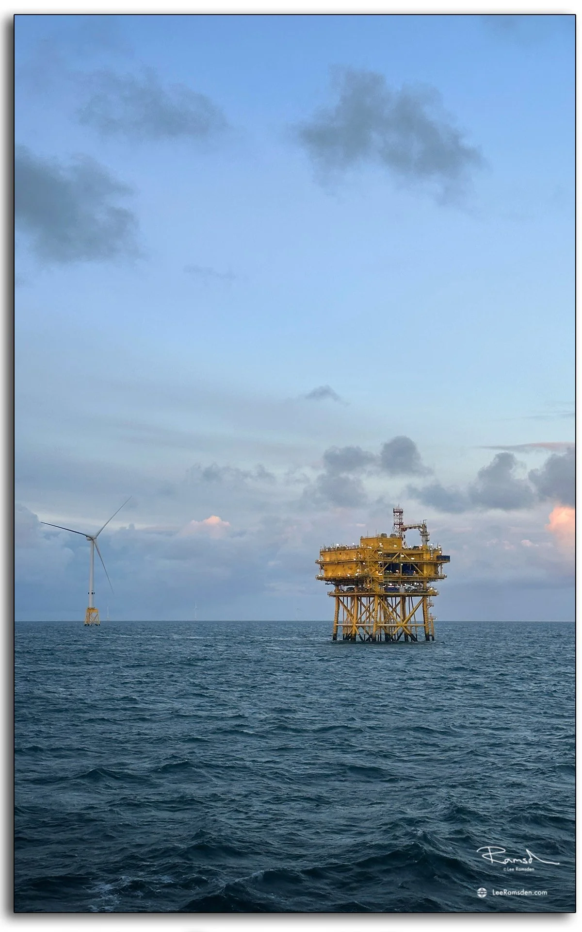 Offshore wind substation framed by open sea and soft clouds, evening light catching the steel structure.
