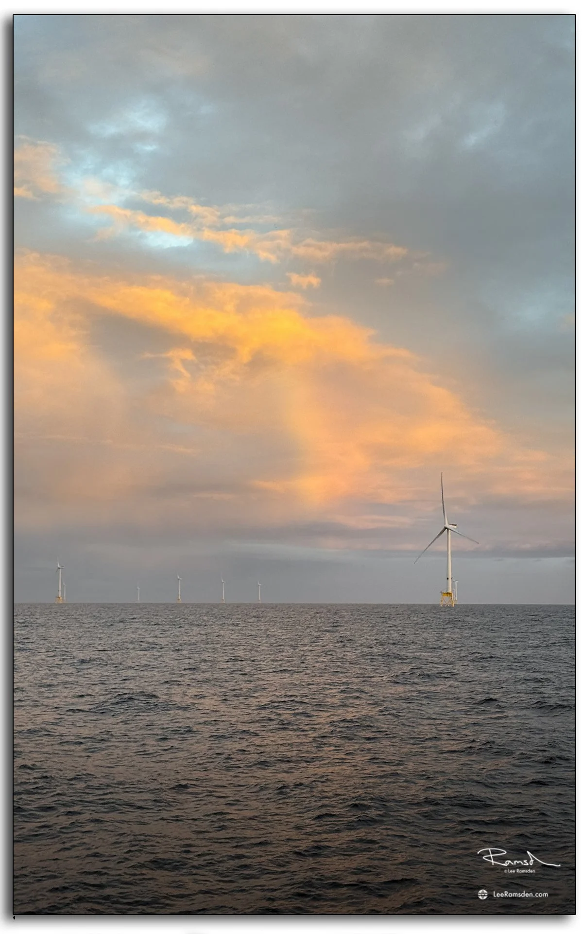 Offshore wind turbine at sunset over the North Sea, with golden clouds highlighting renewable energy at sea.