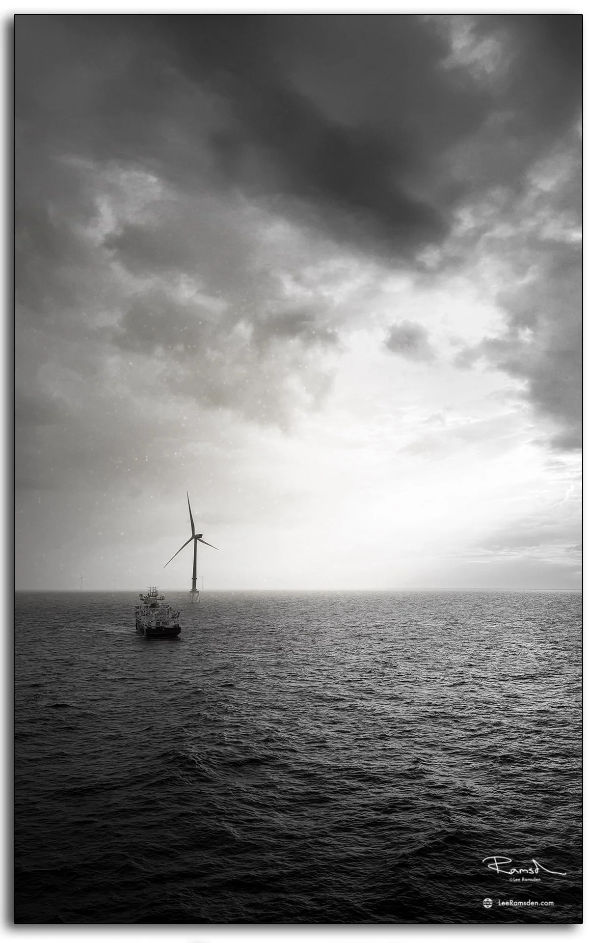 Striking black and white photo of Island Diligence with offshore wind turbine under dramatic skies in the North Sea.