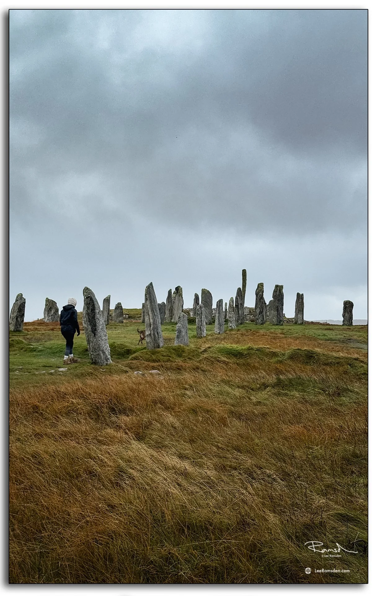 Person walking among the ancient Callanish Standing Stones on the Isle of Lewis, Scotland, surrounded by misty skies and rugged moorland