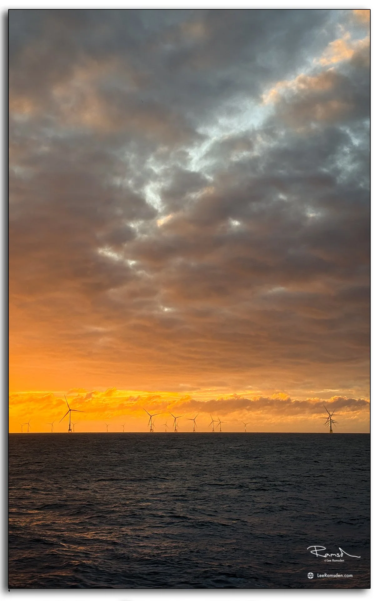 Close view of turbine framed by glowing sunset offshore.