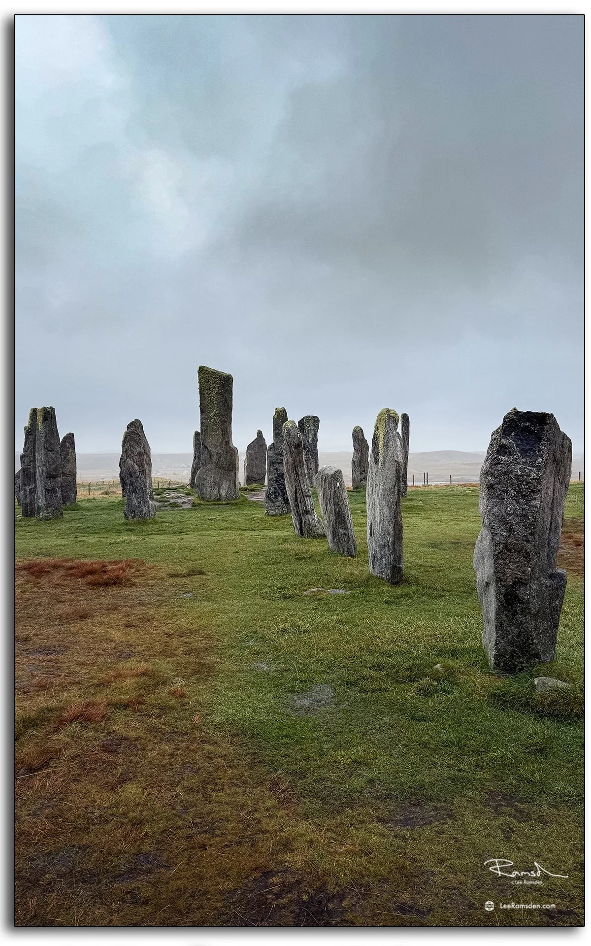 Person walking among the ancient Callanish Standing Stones on the Isle of Lewis, Scotland, surrounded by misty skies and rugged moorland