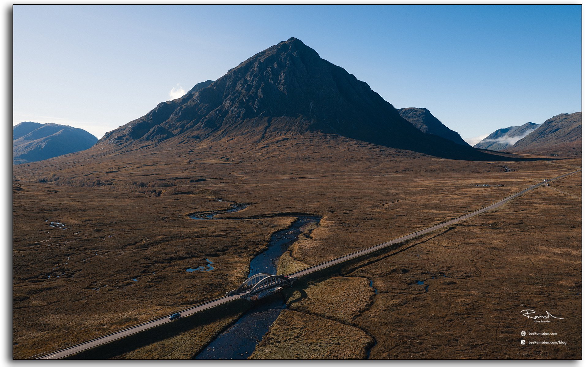 Aerial view of Buachaille Etive Mòr mountain and the River Etive bridge in Glencoe, Scotland, under clear blue skies