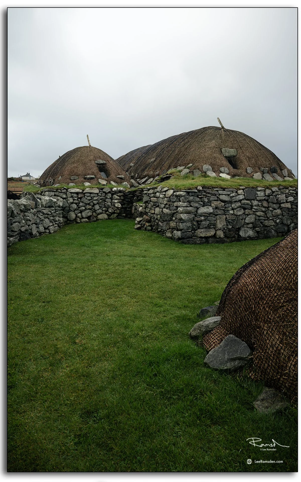 Traditional stone and thatch blackhouses at Gearrannan on the Isle of Lewis, Scotland, showing restored crofting homes surrounded by green grass and moody skies