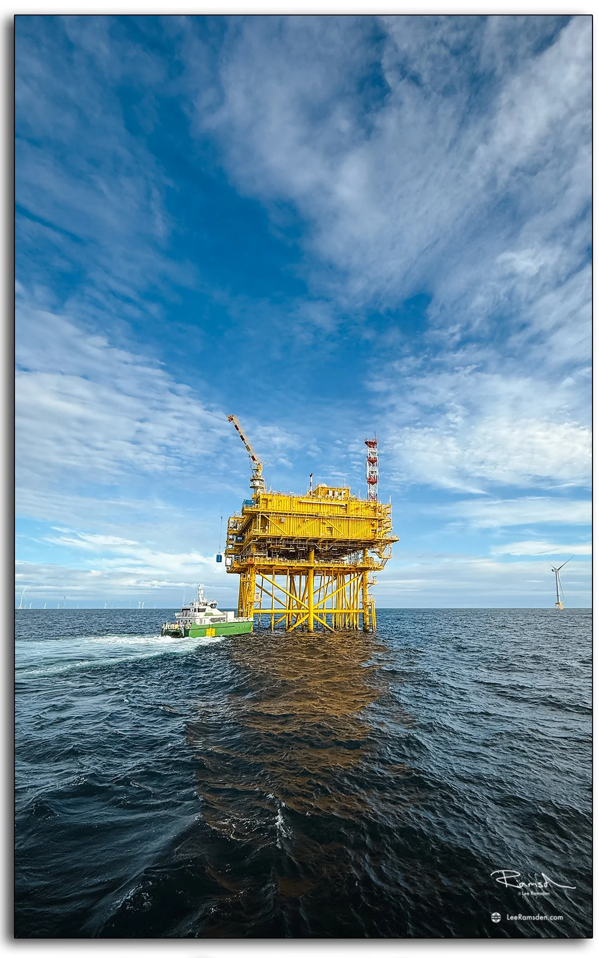 Offshore substation with CTV and wind turbine in background, capturing renewable energy operations in the North Sea.