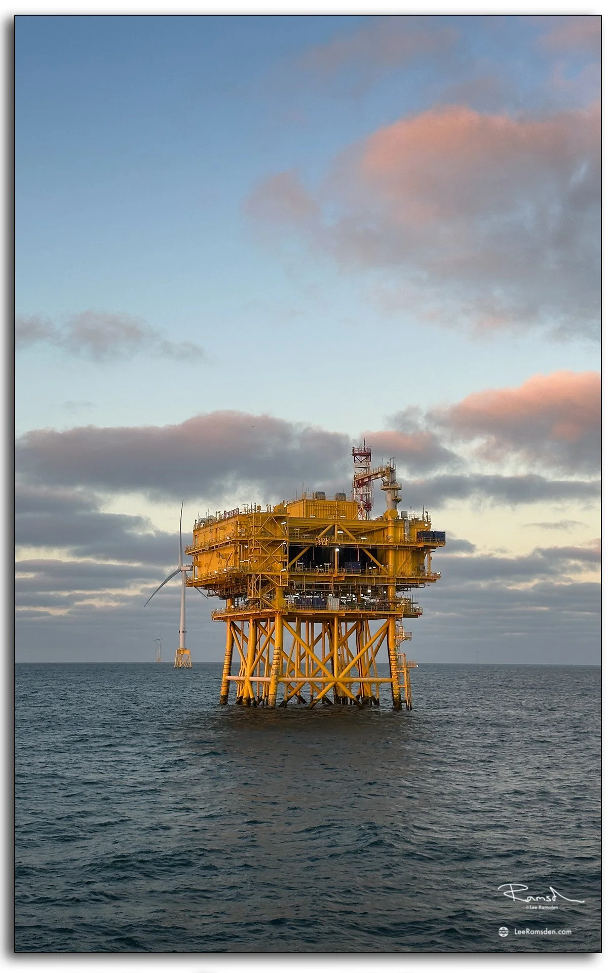 Offshore substation platform at sunset, with warm evening light and turbines in the distance.