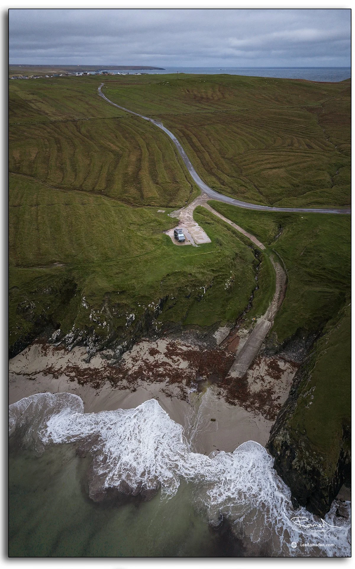 Aerial view of a secluded beach and winding road near the Butt of Lewis, Isle of Lewis, Scotland, showing rugged cliffs and Atlantic waves