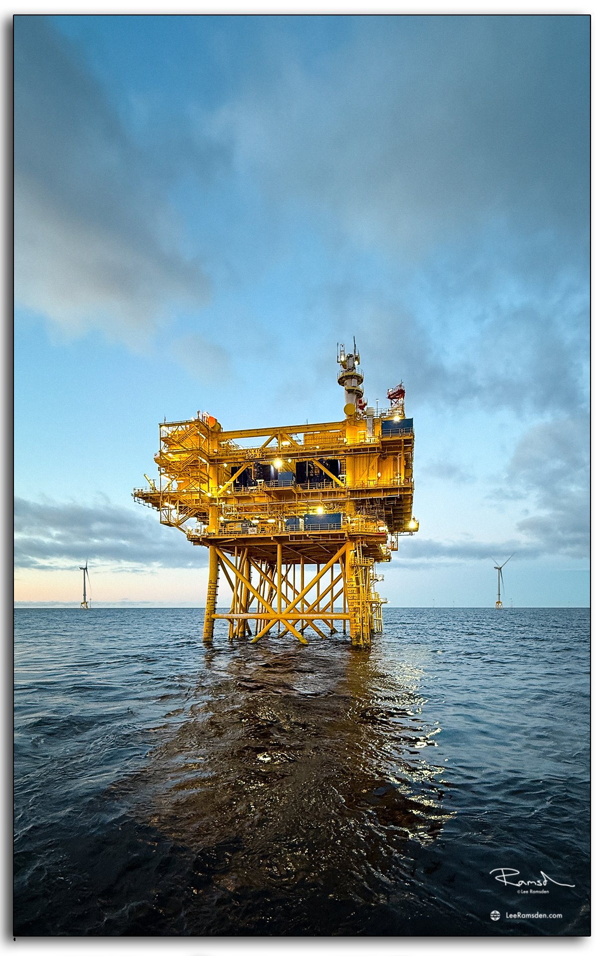 Offshore substation framed against a glowing sky, with wind turbines visible in the distance.