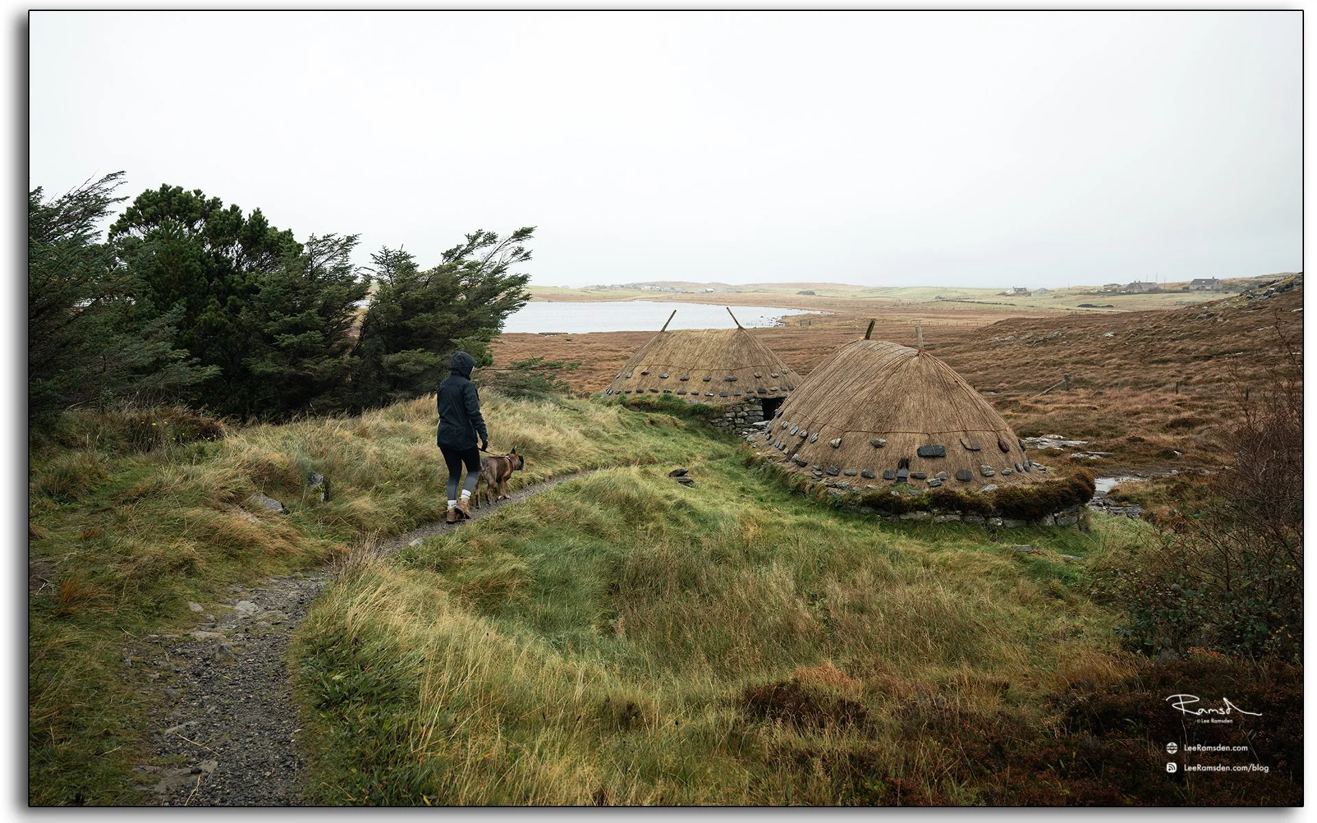 Traditional thatched blackhouses at Arnol on the Isle of Lewis, Scotland, with stone walls beside a flowing stream under grey Hebridean skies