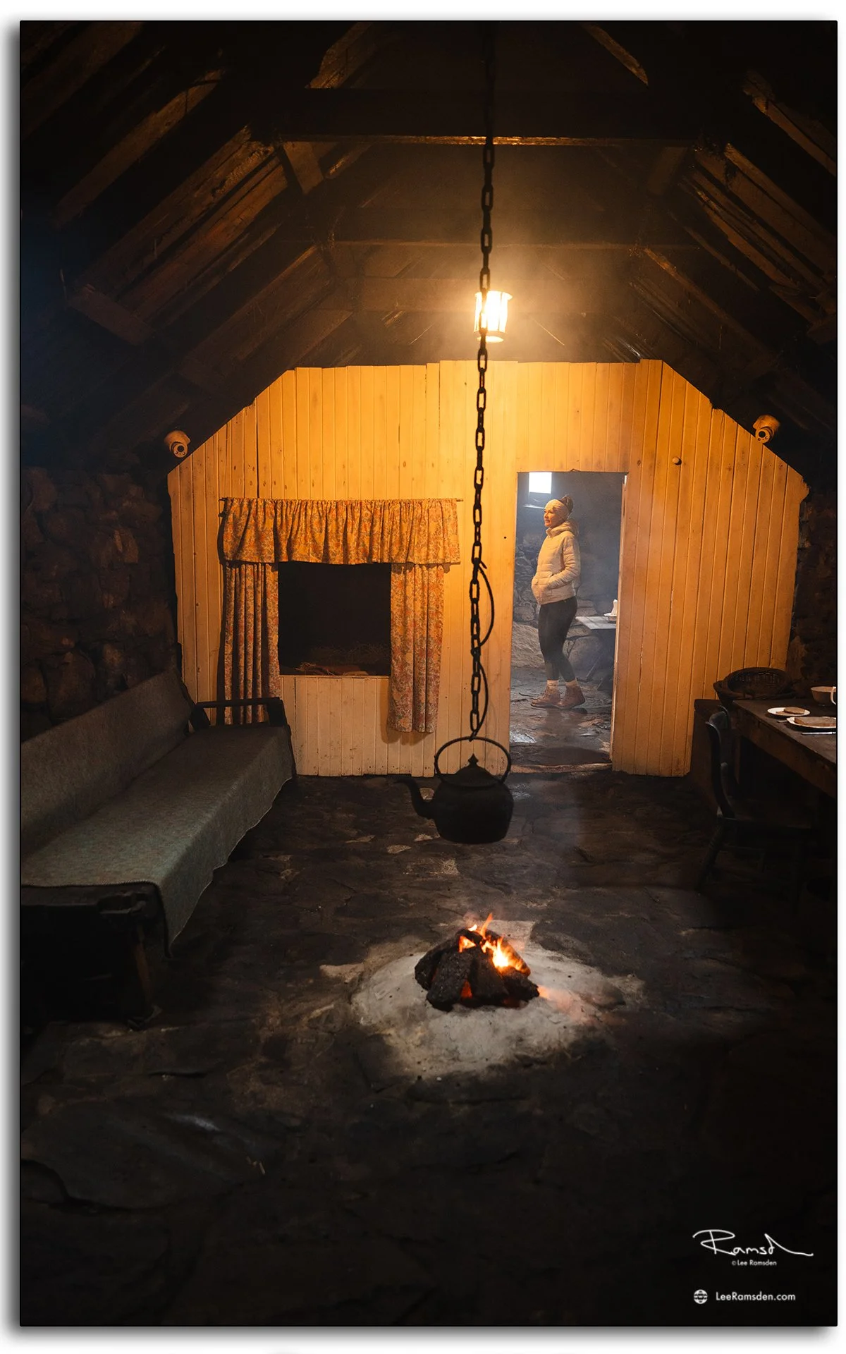 Interior of a traditional blackhouse at Gearrannan on the Isle of Lewis, Scotland, showing an open fire, hanging kettle, and rustic stone-and-wood construction
