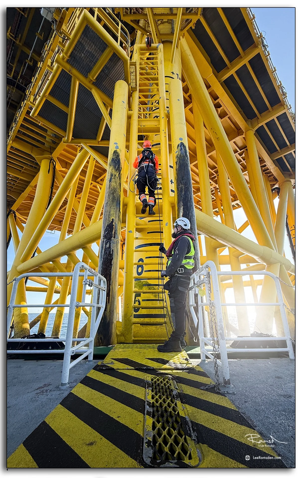 Technician climbing ladder from CTV to platform with rope access safety measures.