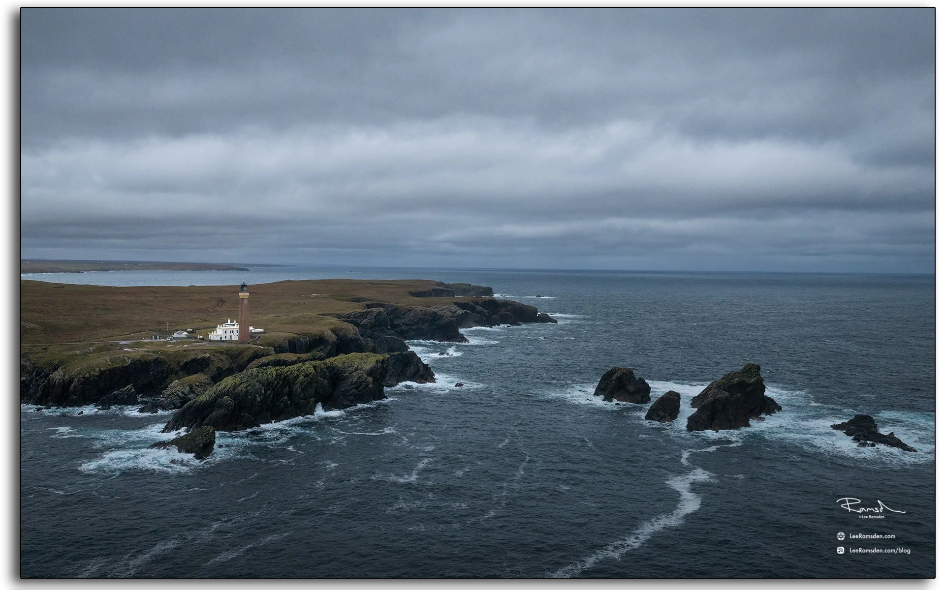 Aerial view of the Butt of Lewis lighthouse on the Isle of Lewis, Scotland, surrounded by dramatic cliffs and crashing Atlantic waves under moody skies.