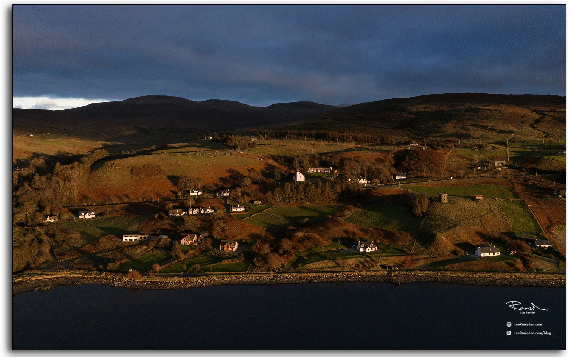 Aerial view of Uig village on the Isle of Skye, Scotland, during sunset, with warm golden light over fields, cottages, and coastal hills