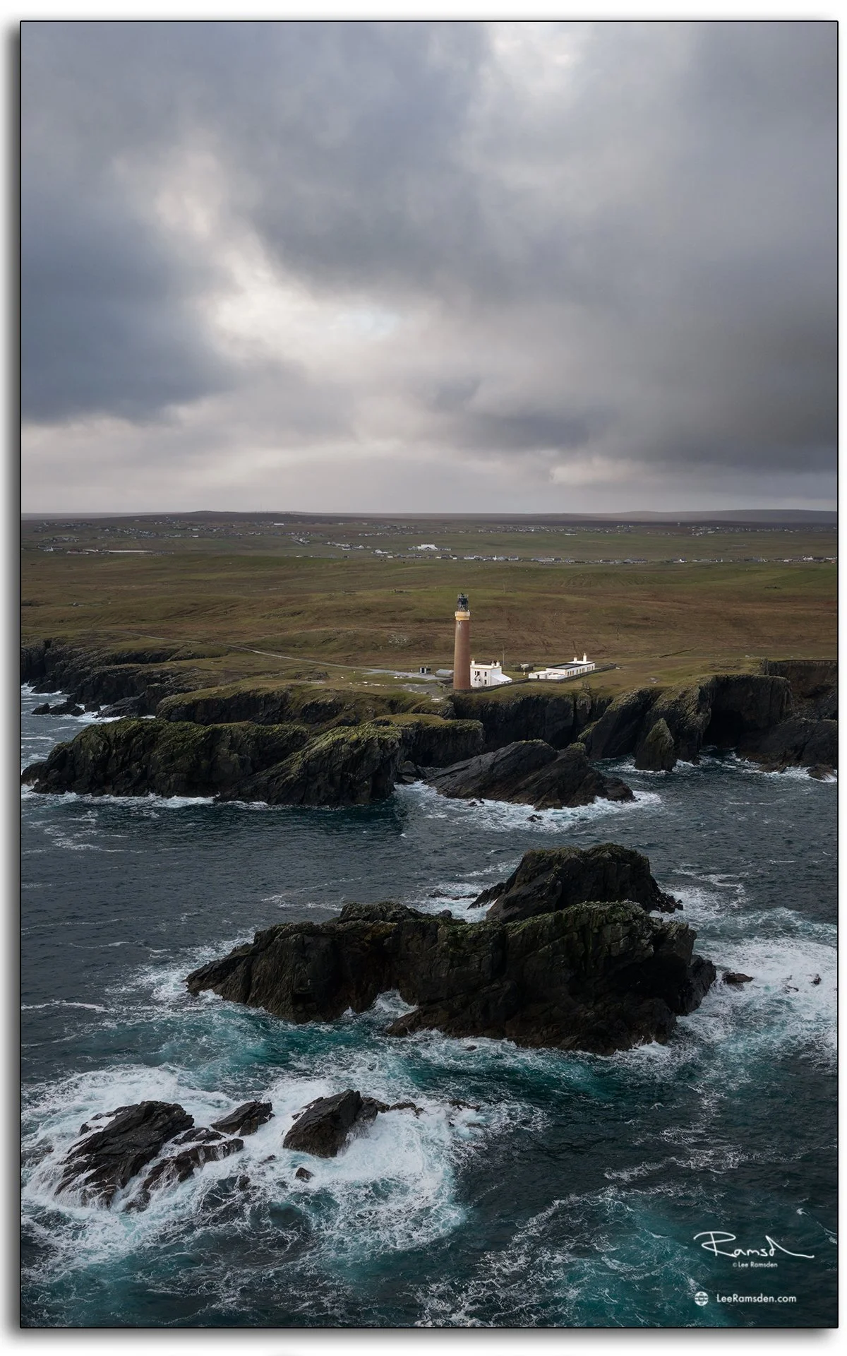 Aerial view of the Butt of Lewis lighthouse on the Isle of Lewis, Scotland, surrounded by dramatic cliffs and crashing Atlantic waves under moody skies.