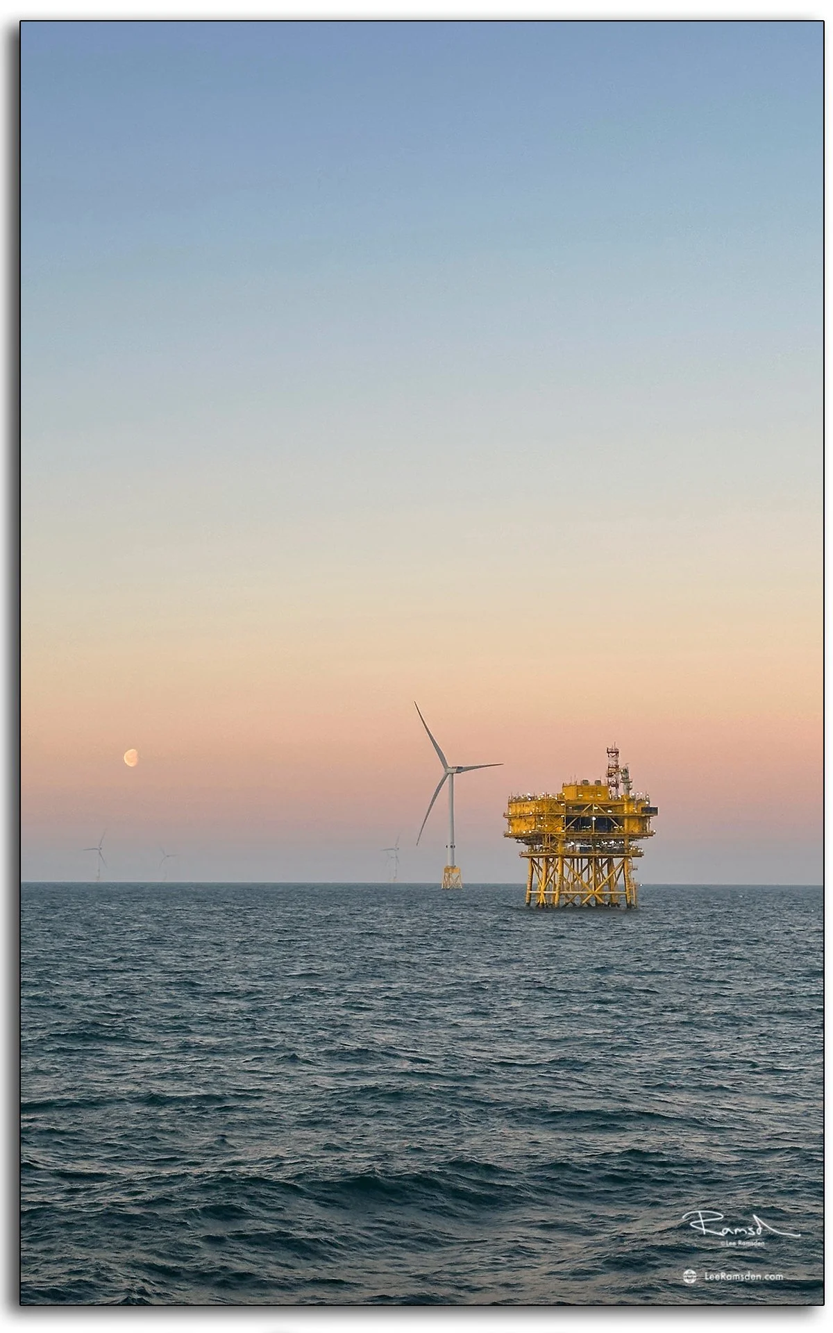 Offshore substation and wind turbine at sunset with pastel sky and calm sea.