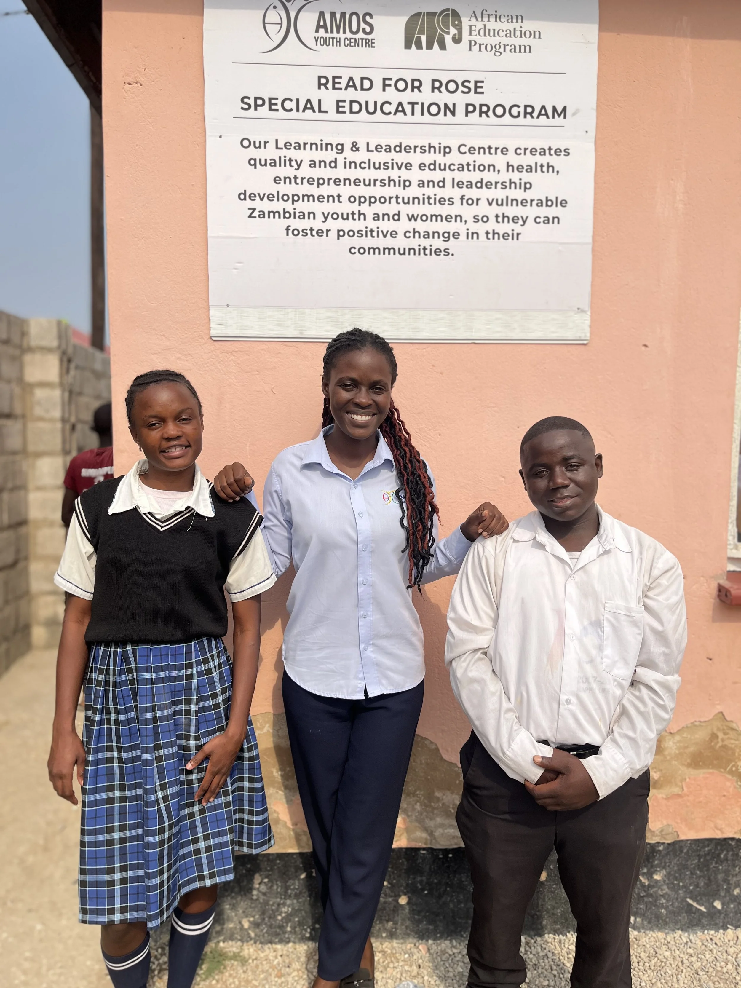 A Zambian teacher stands between a boy and a girl, two of her students now attending boarding school to finish grade 12.