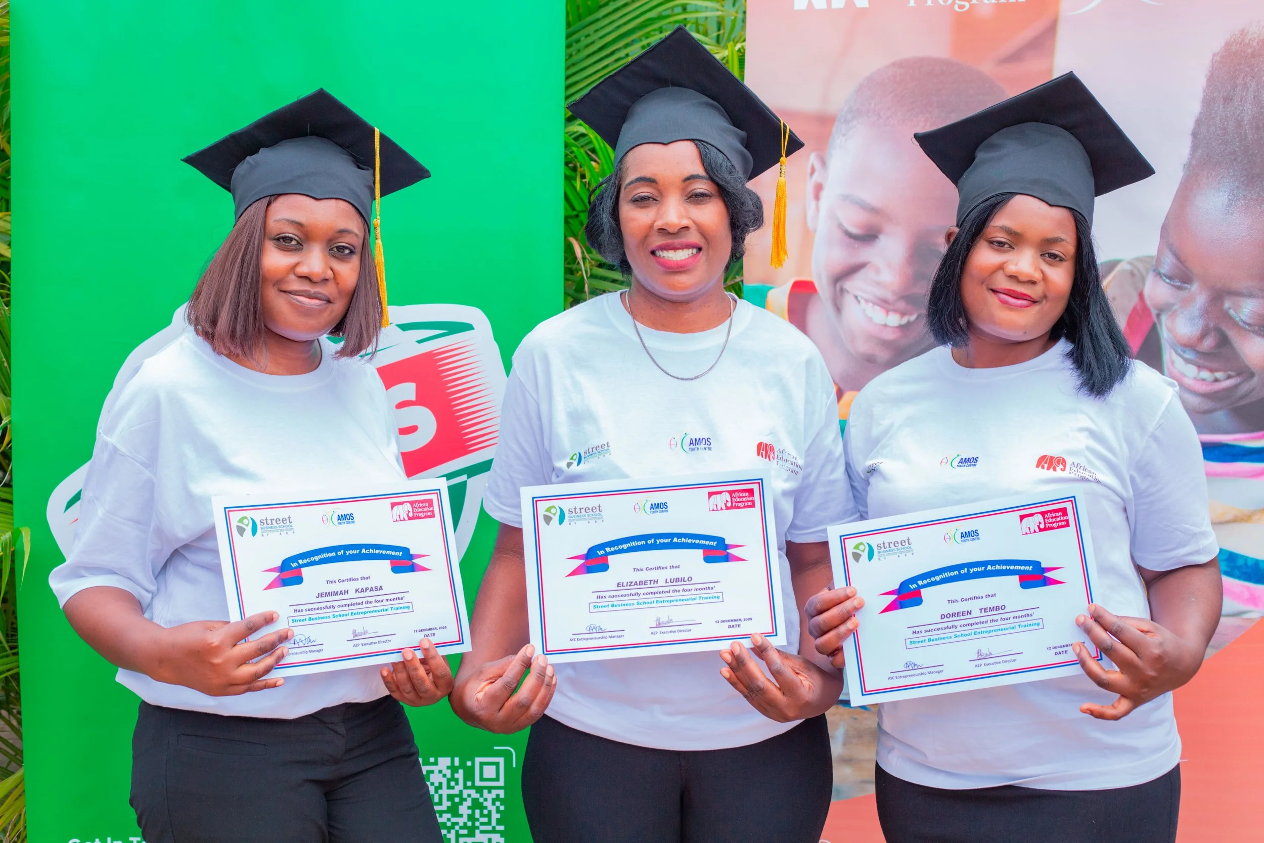 A photo of three Zambian women wearing graduation caps and holding graducation diplomas from AYC's Women's Business Training.