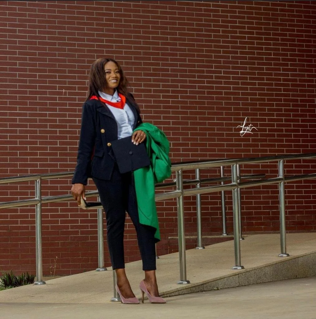 Patricia stands in front of a building with her graduation cap and gown in her hand