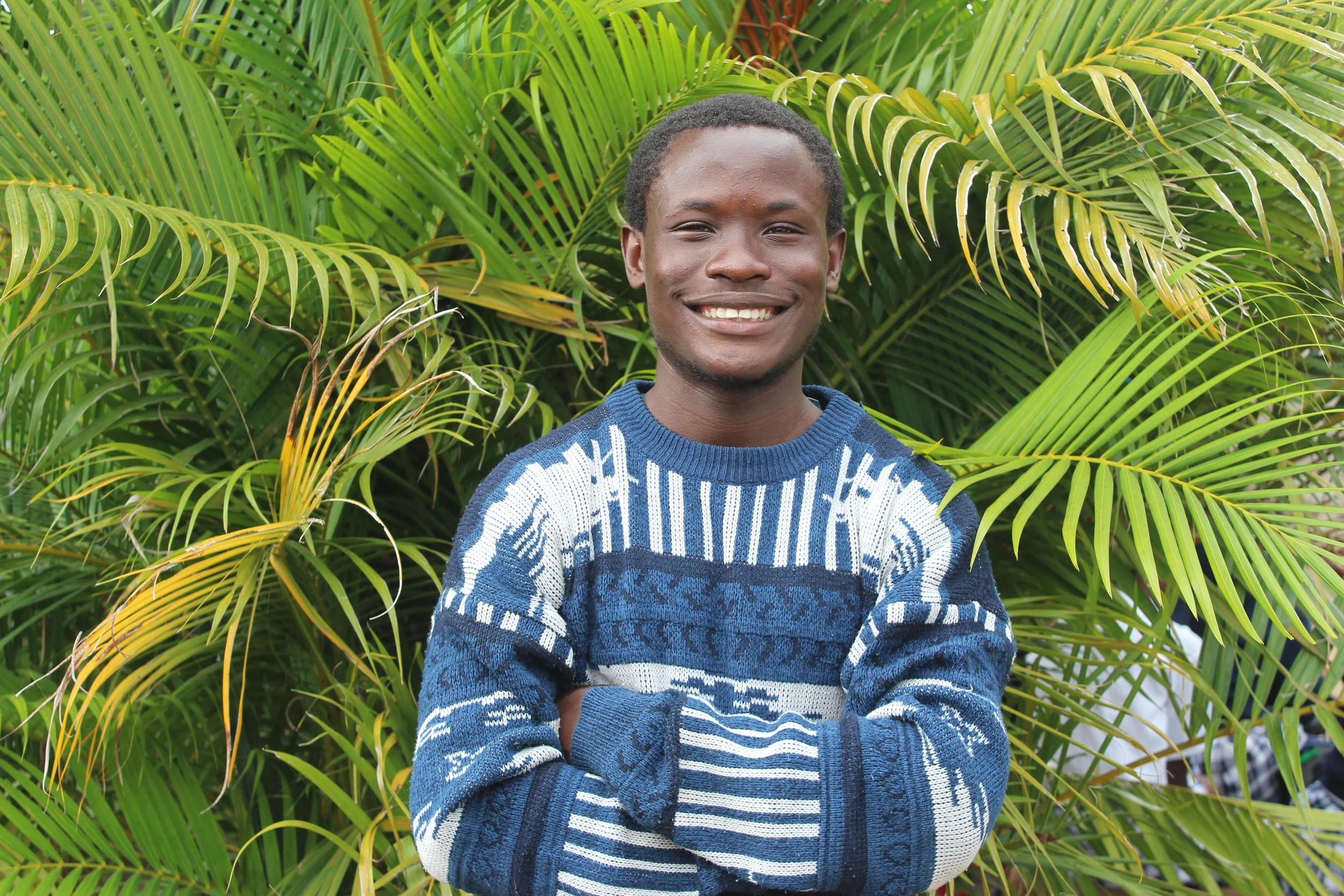 A Zambian male smiles for the camera wearing a blue striped sweater