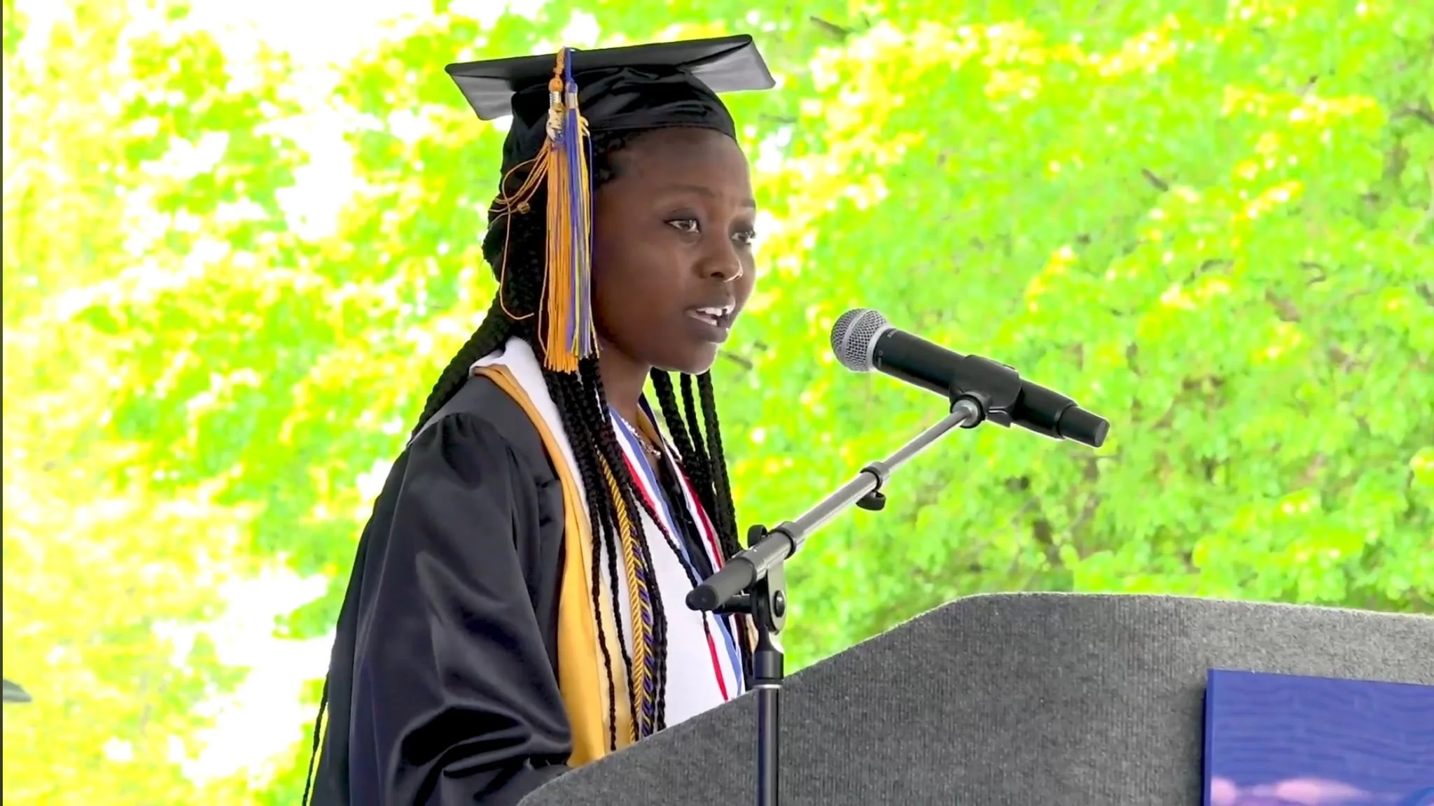 Picture of a Zambian girl giving at a podium wearing a cap and gown.