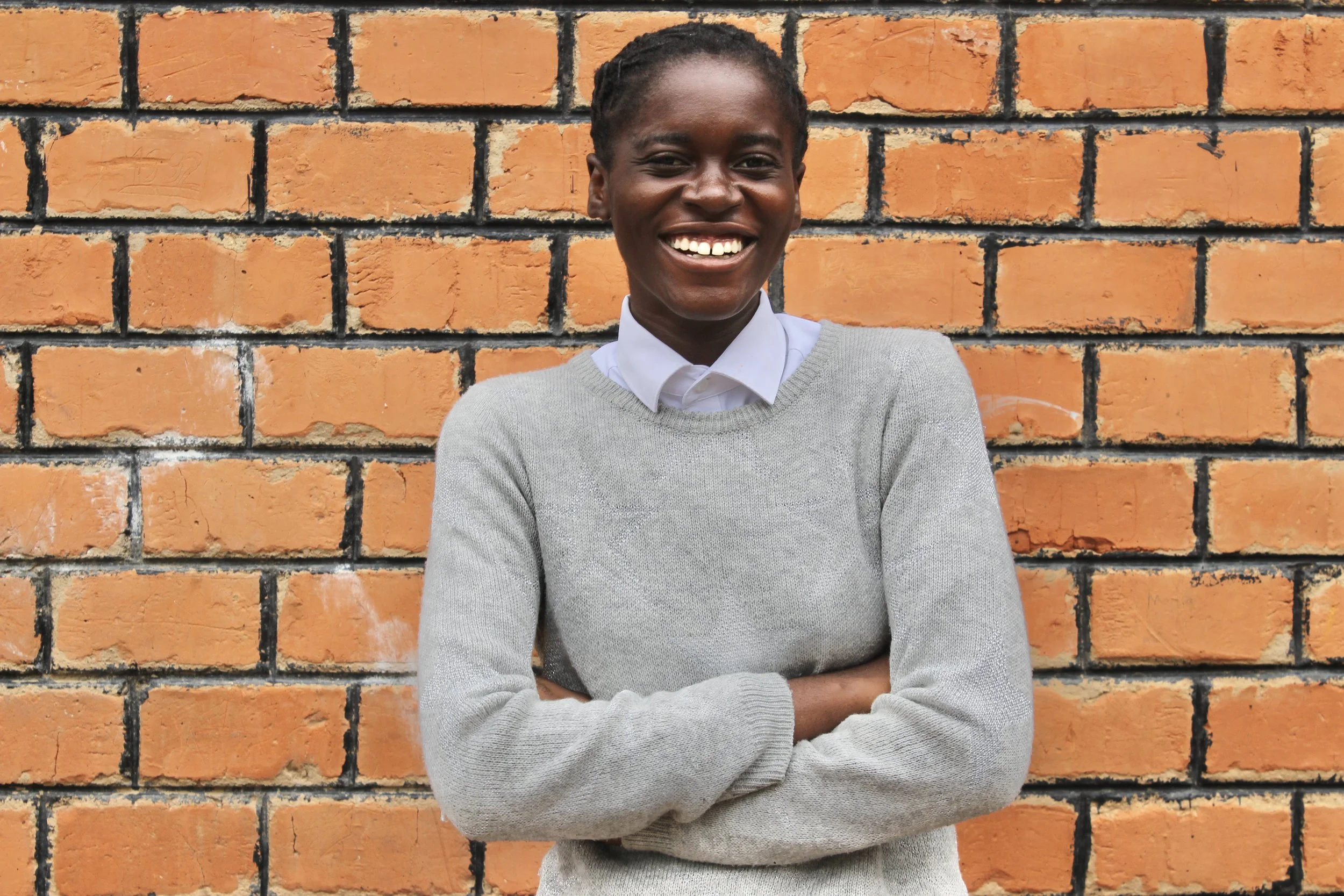 Young Zambian girl wearing a grey sweater smiles at the camera
