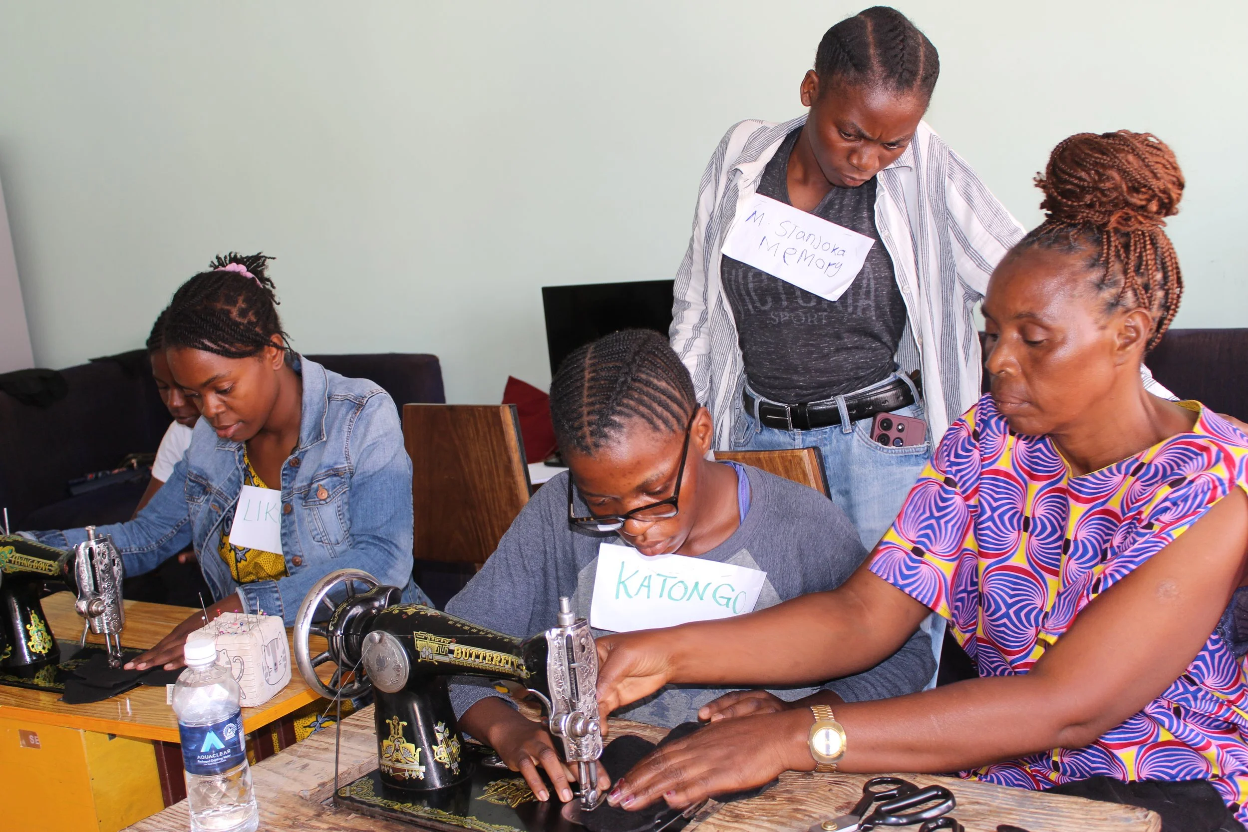 Zambian women stand around a sewing machine during tailoring classes