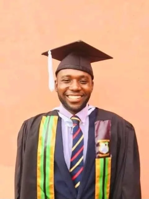 A Zambian man smile in his university cap and gown at graduation.