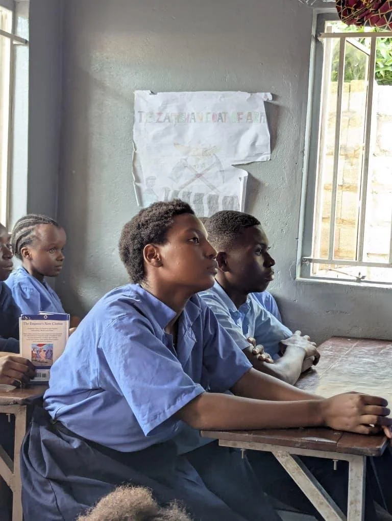 Several Zambian children wearing their blue school uniforms look at the teacher.