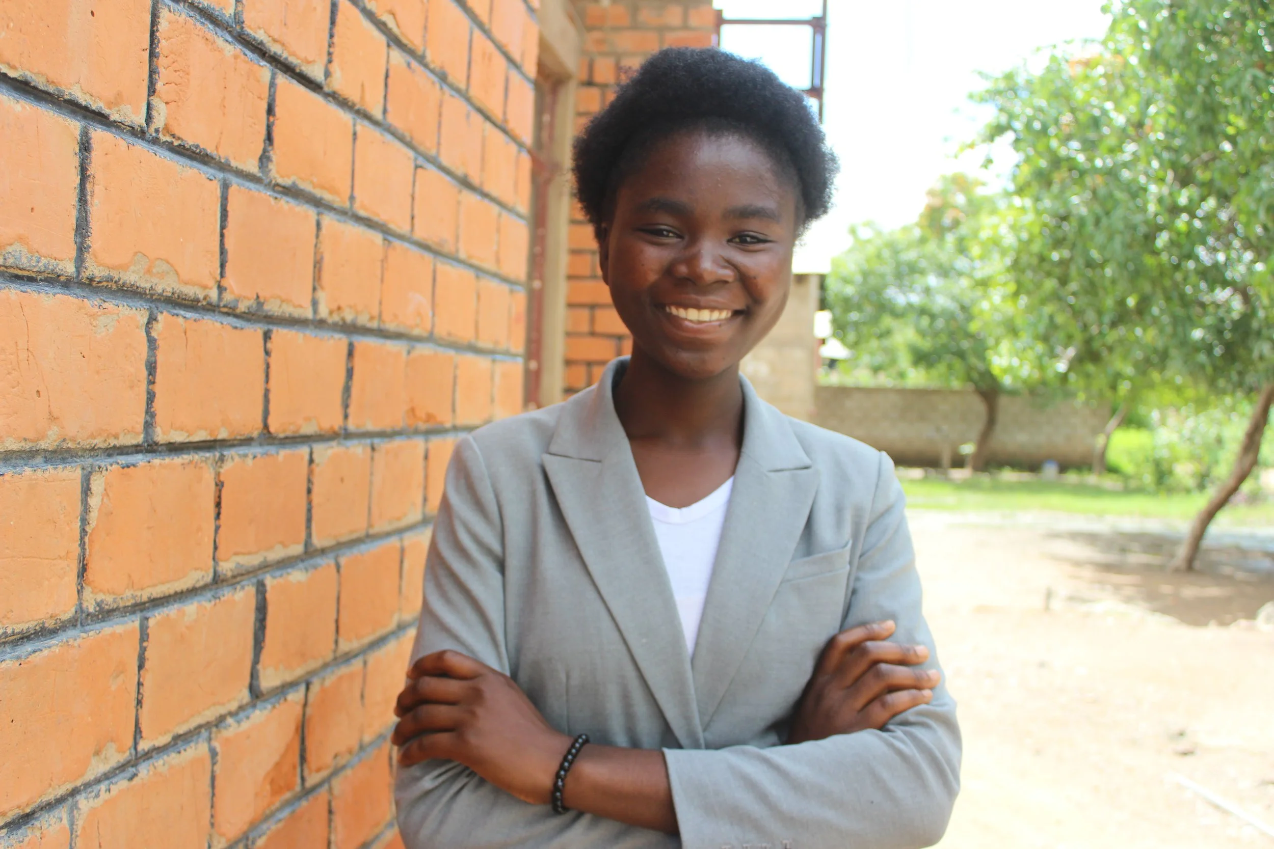 A young Zambian female wearing a grey blazer and white shirt smiles for the camera.