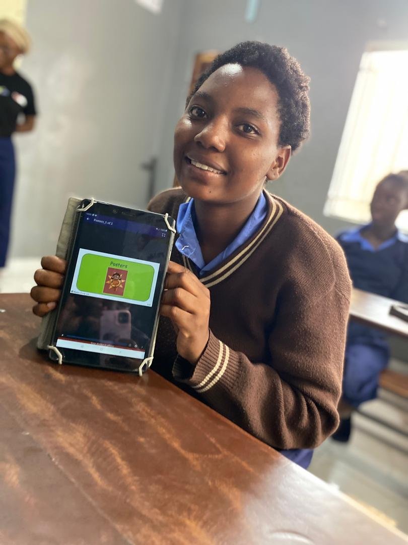 A young Zambian girl wearing a brown shirt holds up a tablet computer.