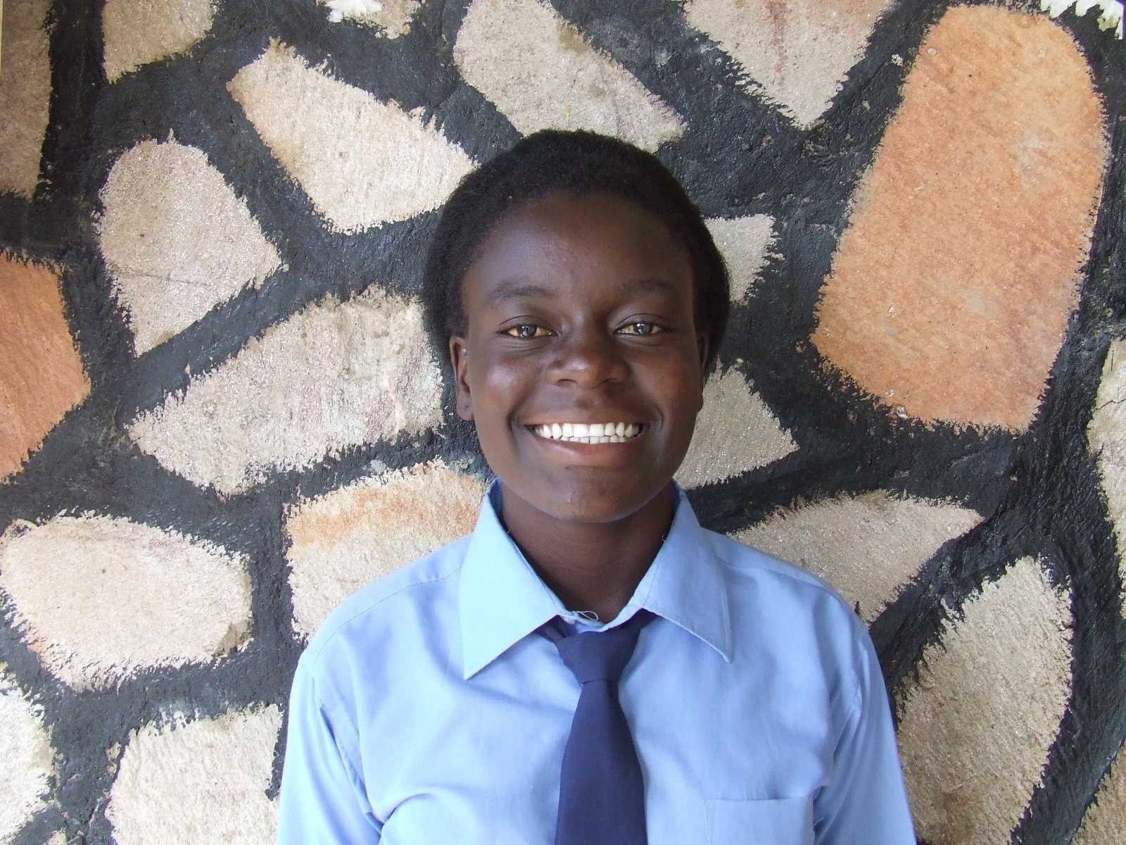 A young Zambian girl smiles for the camera wearing a blue school uniform.