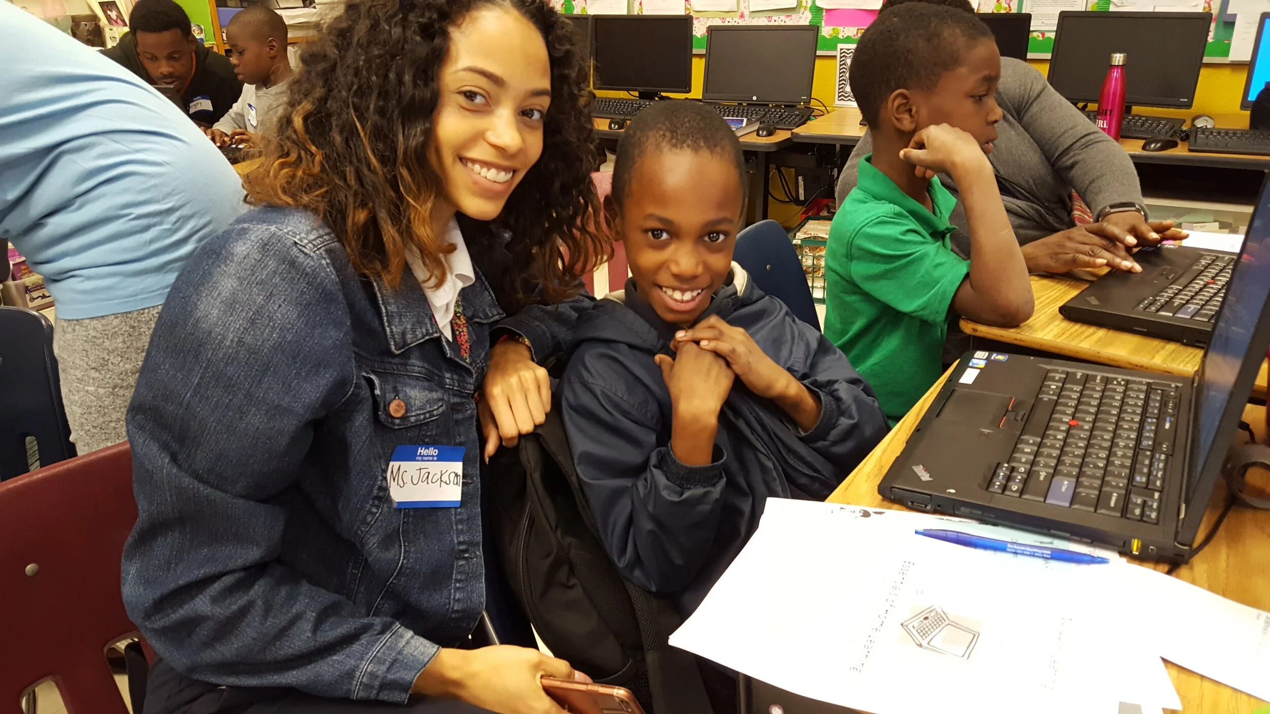 Inspiredu volunteer works with students using laptops in a classroom.