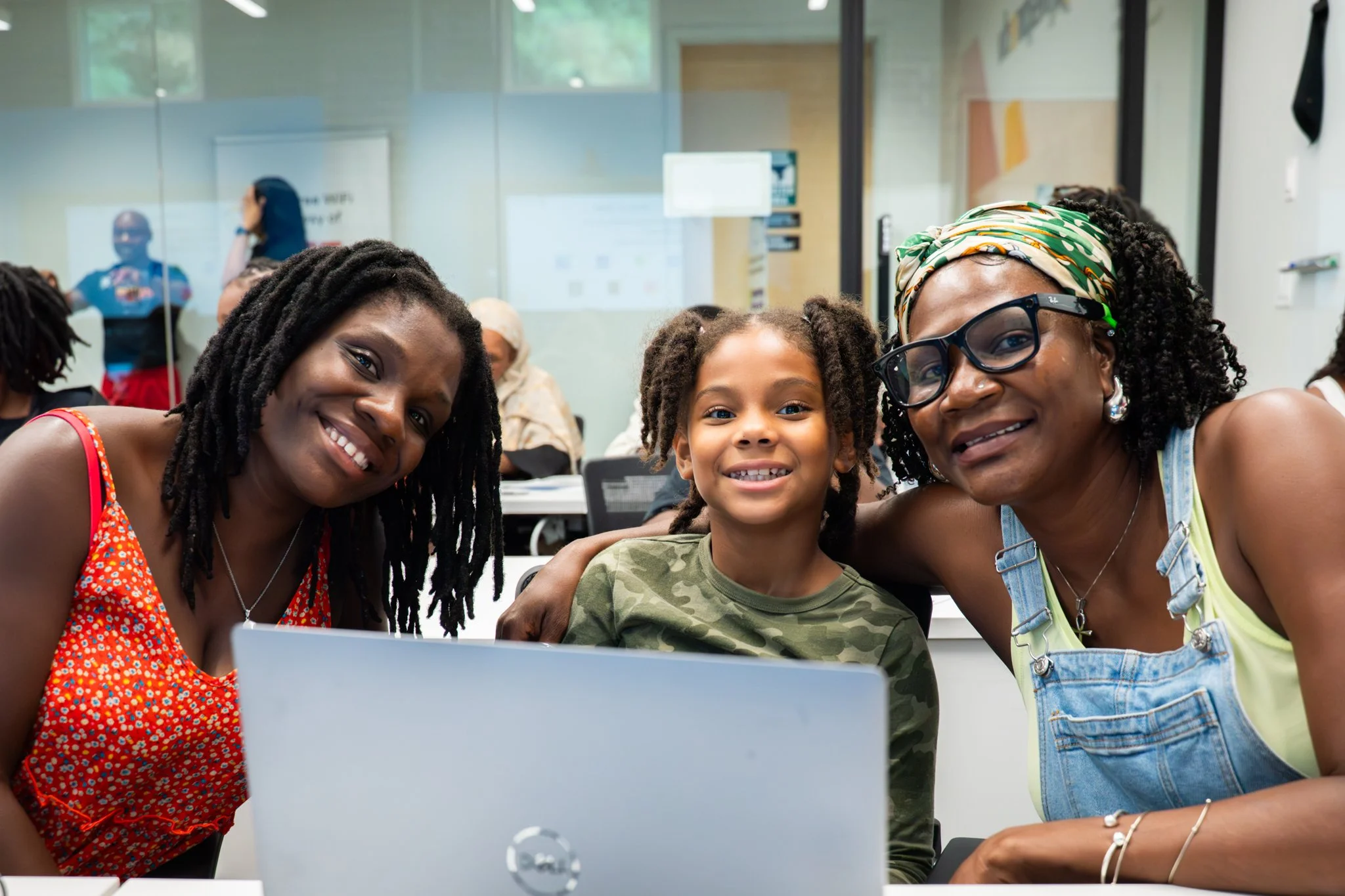 Family members participating in an Inspiredu digital literacy program, smiling together while using a laptop.